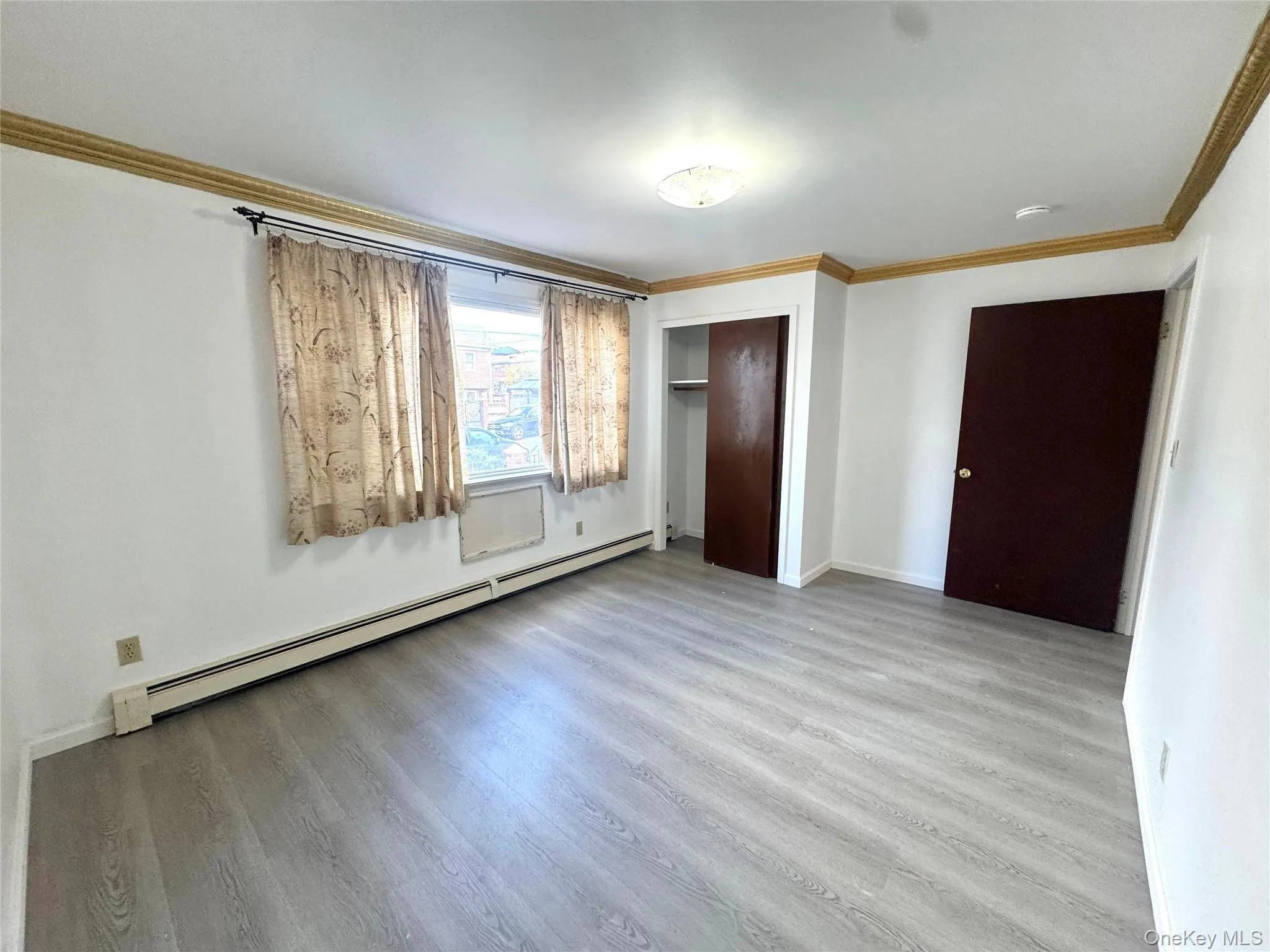 Unfurnished bedroom with crown molding, a baseboard radiator, a closet, and light wood-style floors Unfurnished bedroom with crown molding, a baseboard radiator, a closet, and light wood-style floors