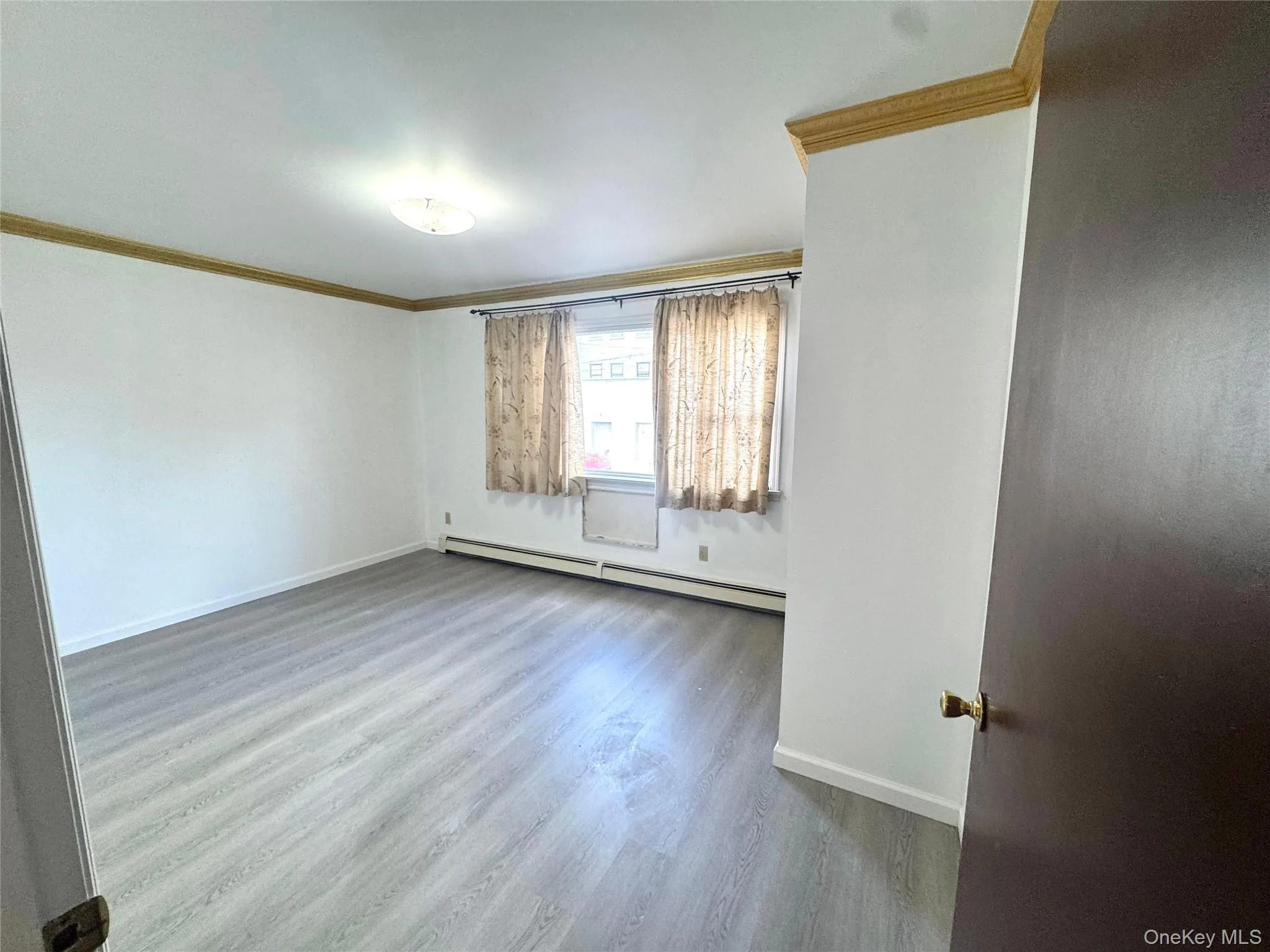 Unfurnished room featuring crown molding, wood finished floors, and a baseboard radiator Unfurnished room featuring crown molding, wood finished floors, and a baseboard radiator