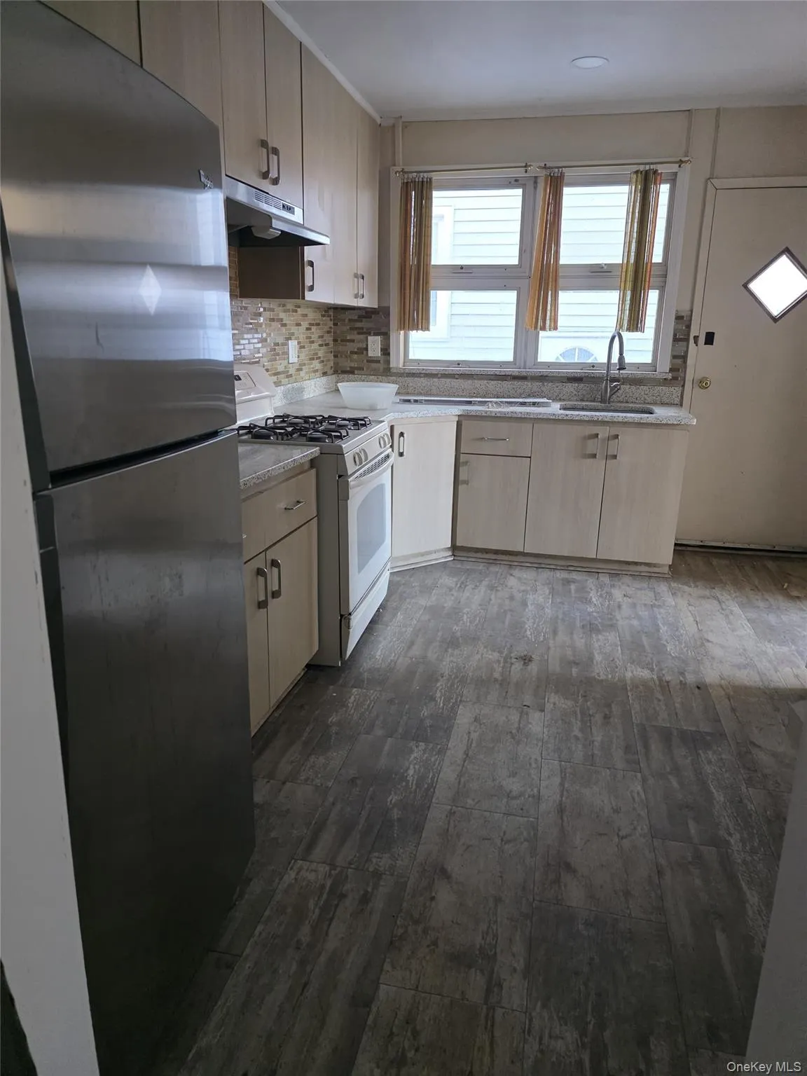 Kitchen with light brown cabinetry, freestanding refrigerator, gas range gas stove, dark wood finished floors, and decorative backsplash Kitchen with light brown cabinetry, freestanding refrigerator, gas range gas stove, dark wood finished floors, and decorative backsplash