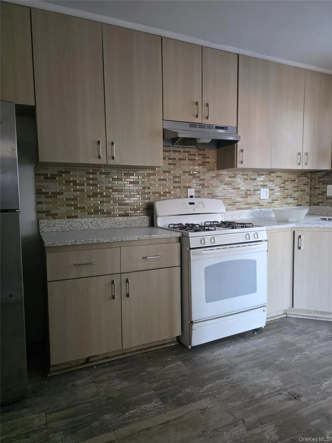 Kitchen featuring white range with gas stovetop, light brown cabinetry, tasteful backsplash, and under cabinet range hood Kitchen featuring white range with gas stovetop, light brown cabinetry, tasteful backsplash, and under cabinet range hood
