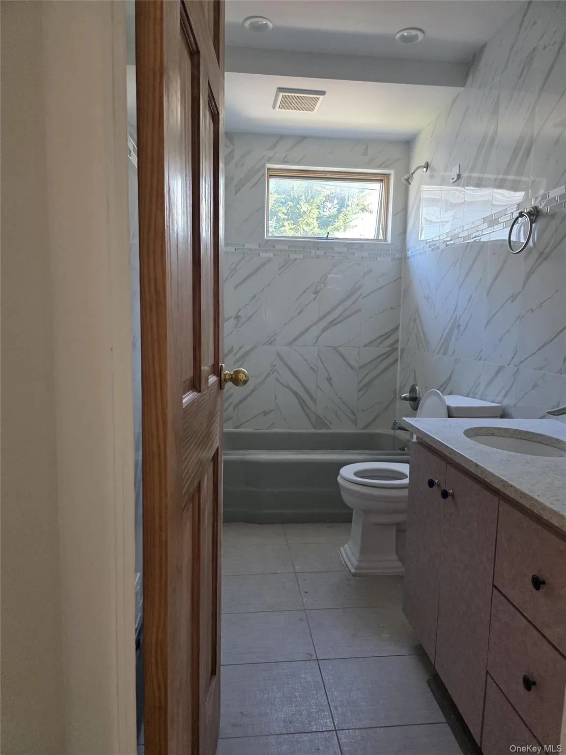 Bathroom featuring vanity, shower combination, light tile patterned floors, and tile walls Bathroom featuring vanity, shower combination, light tile patterned floors, and tile walls