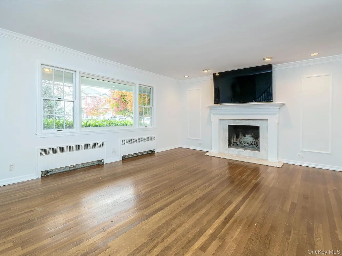 Unfurnished living room featuring radiator, ornamental molding, hardwood / wood-style floors, a high end fireplace, and recessed lighting Unfurnished living room featuring radiator, ornamental molding, hardwood / wood-style floors, a high end fireplace, and recessed lighting