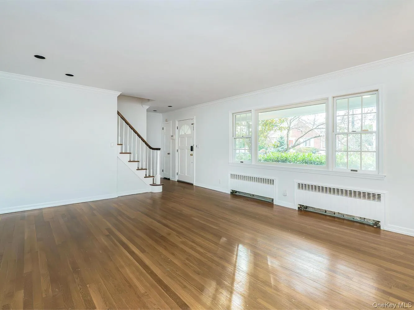 Unfurnished living room with crown molding, stairway, radiator, and dark wood-type flooring Unfurnished living room with crown molding, stairway, radiator, and dark wood-type flooring