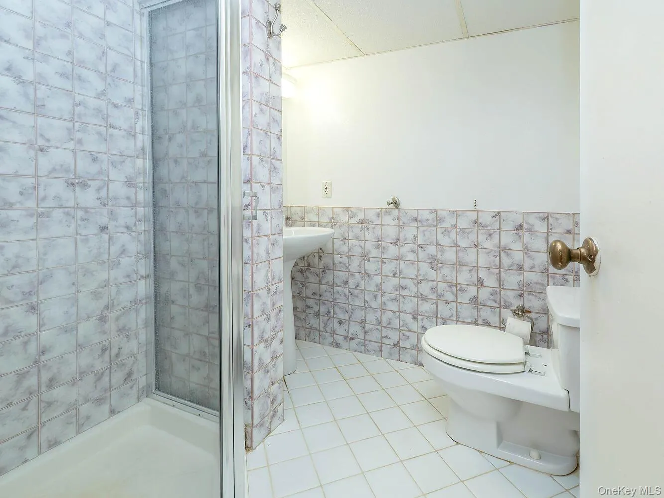 Full bathroom with tile walls, light tile patterned floors, wainscoting, and a stall shower Full bathroom with tile walls, light tile patterned floors, wainscoting, and a stall shower