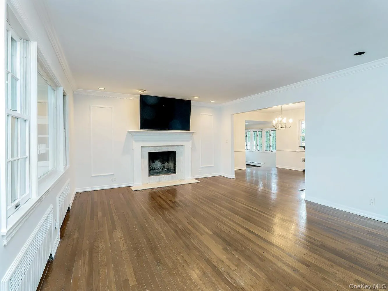 Unfurnished living room featuring radiator, dark wood-style floors, crown molding, a premium fireplace, and a chandelier Unfurnished living room featuring radiator, dark wood-style floors, crown molding, a premium fireplace, and a chandelier