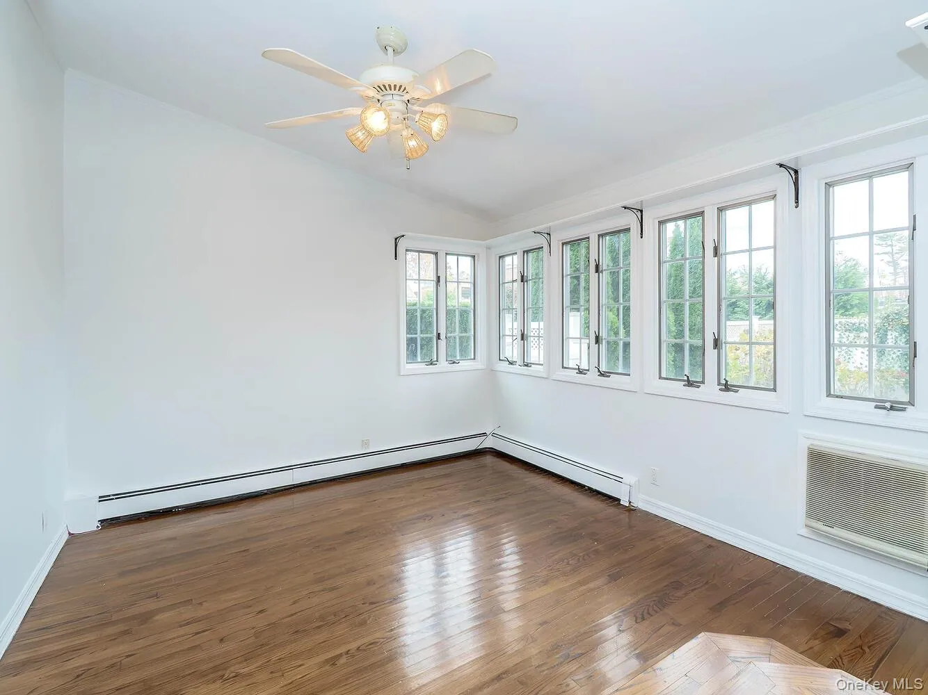 Empty room featuring hardwood / wood-style flooring, a baseboard heating unit, a ceiling fan, lofted ceiling, and an AC wall unit Empty room featuring hardwood / wood-style flooring, a baseboard heating unit, a ceiling fan, lofted ceiling, and an AC wall unit