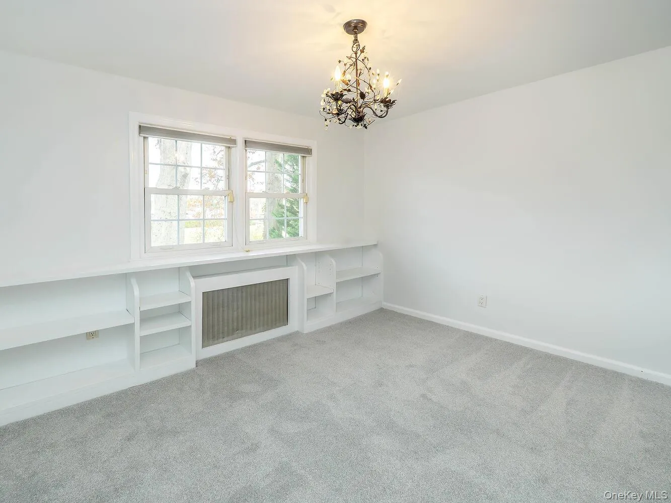 Unfurnished living room featuring radiator heating unit, light carpet, and a chandelier Unfurnished living room featuring radiator heating unit, light carpet, and a chandelier