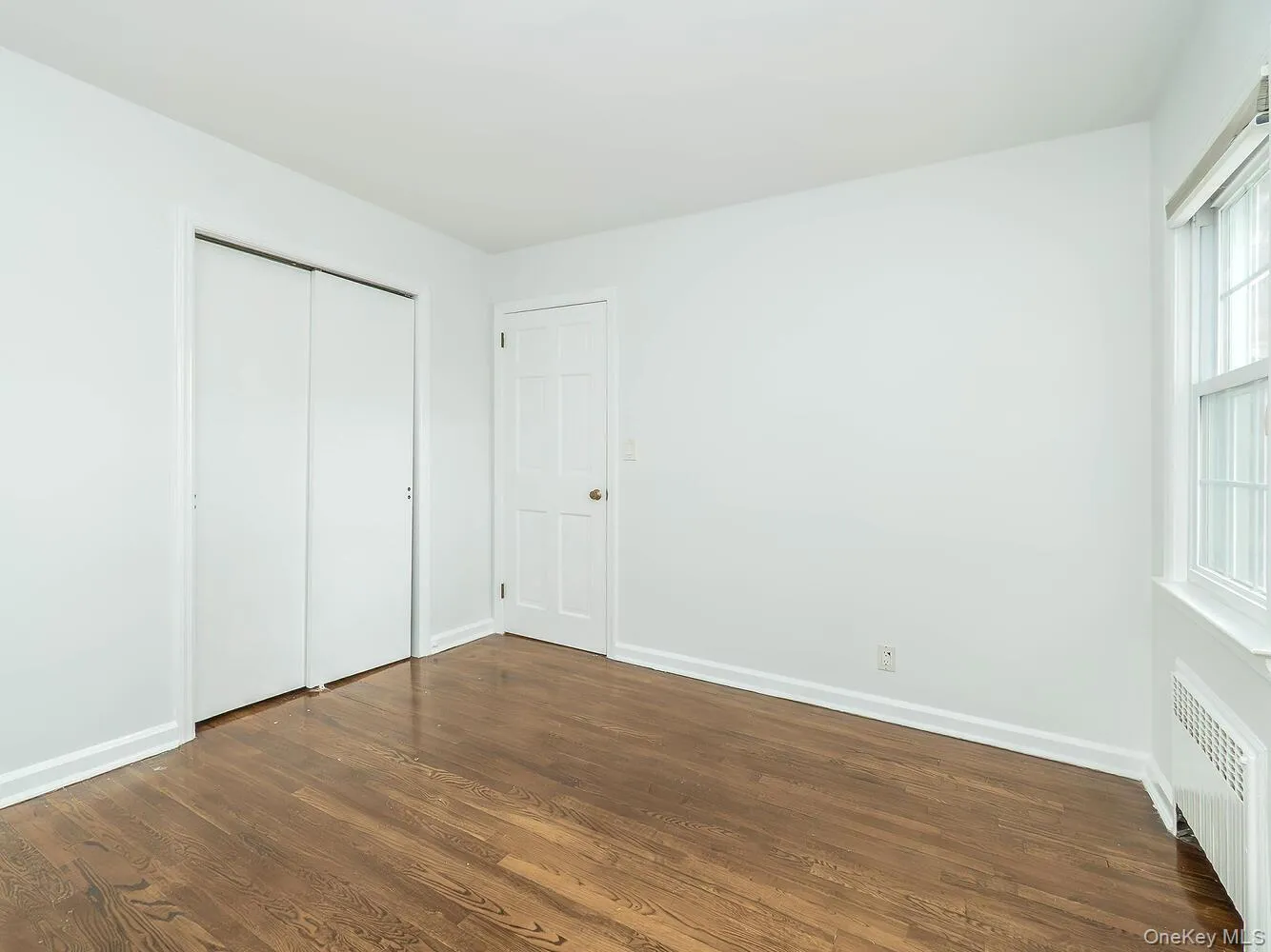 Unfurnished bedroom featuring radiator, dark wood-style floors, and a closet Unfurnished bedroom featuring radiator, dark wood-style floors, and a closet