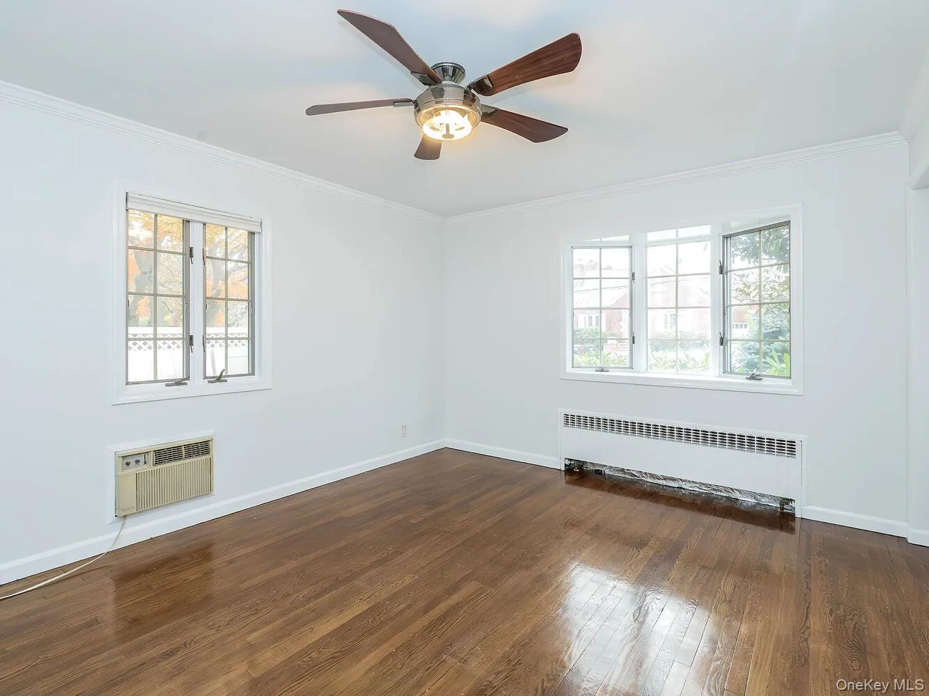 Unfurnished room featuring crown molding, radiator, dark wood-type flooring, ceiling fan, and a wall unit AC Unfurnished room featuring crown molding, radiator, dark wood-type flooring, ceiling fan, and a wall unit AC