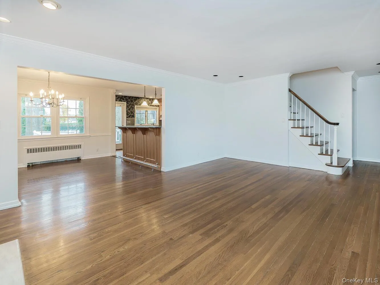 Unfurnished living room featuring radiator, crown molding, stairway, dark wood finished floors, and a chandelier Unfurnished living room featuring radiator, crown molding, stairway, dark wood finished floors, and a chandelier