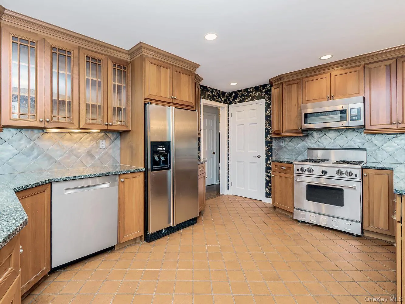 Kitchen featuring dark stone counters, backsplash, appliances with stainless steel finishes, brown cabinetry, and recessed lighting Kitchen featuring dark stone counters, backsplash, appliances with stainless steel finishes, brown cabinetry, and recessed lighting