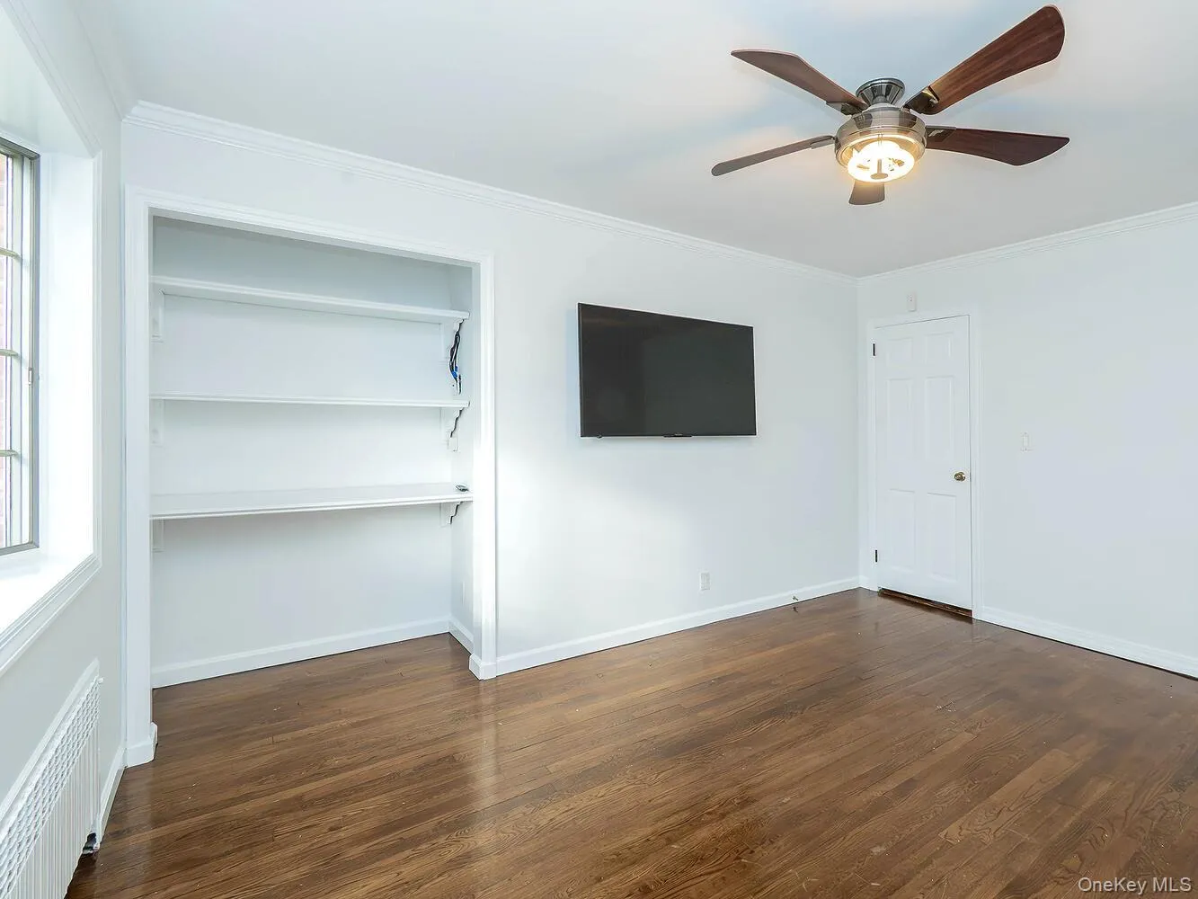 Unfurnished bedroom featuring ornamental molding, radiator, dark wood-style flooring, a ceiling fan, and a closet Unfurnished bedroom featuring ornamental molding, radiator, dark wood-style flooring, a ceiling fan, and a closet