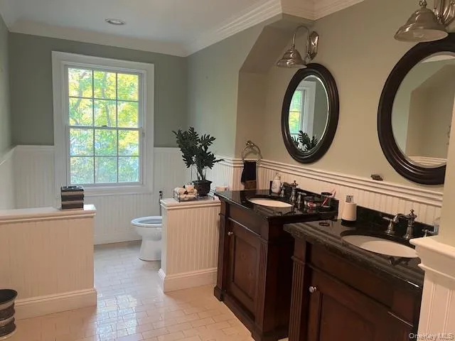 Bathroom with wainscoting, plenty of natural light, ornamental molding, two vanities, and light tile patterned floors Bathroom with wainscoting, plenty of natural light, ornamental molding, two vanities, and light tile patterned floors