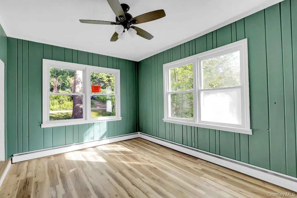 Unfurnished room with wood finished floors, a baseboard heating unit, a ceiling fan, and wood walls Unfurnished room with wood finished floors, a baseboard heating unit, a ceiling fan, and wood walls