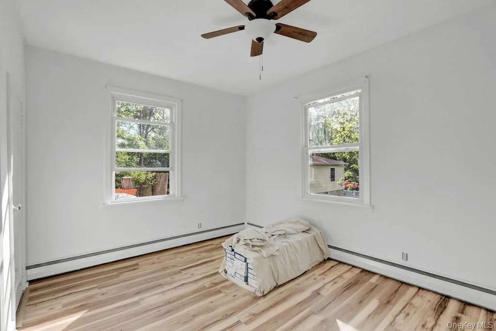Empty room with a baseboard radiator, a baseboard heating unit, light wood-style floors, and healthy amount of natural light Empty room with a baseboard radiator, a baseboard heating unit, light wood-style floors, and healthy amount of natural light