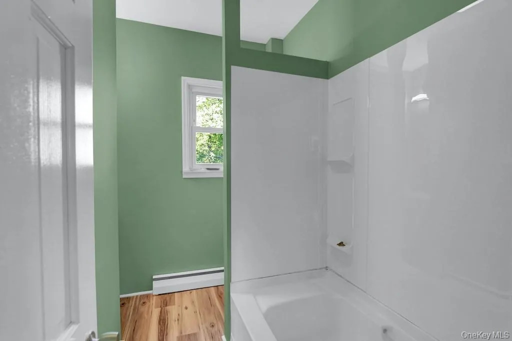 Full bathroom with baseboard heating, light wood-style floors, and shower / washtub combination Full bathroom with baseboard heating, light wood-style floors, and shower / washtub combination
