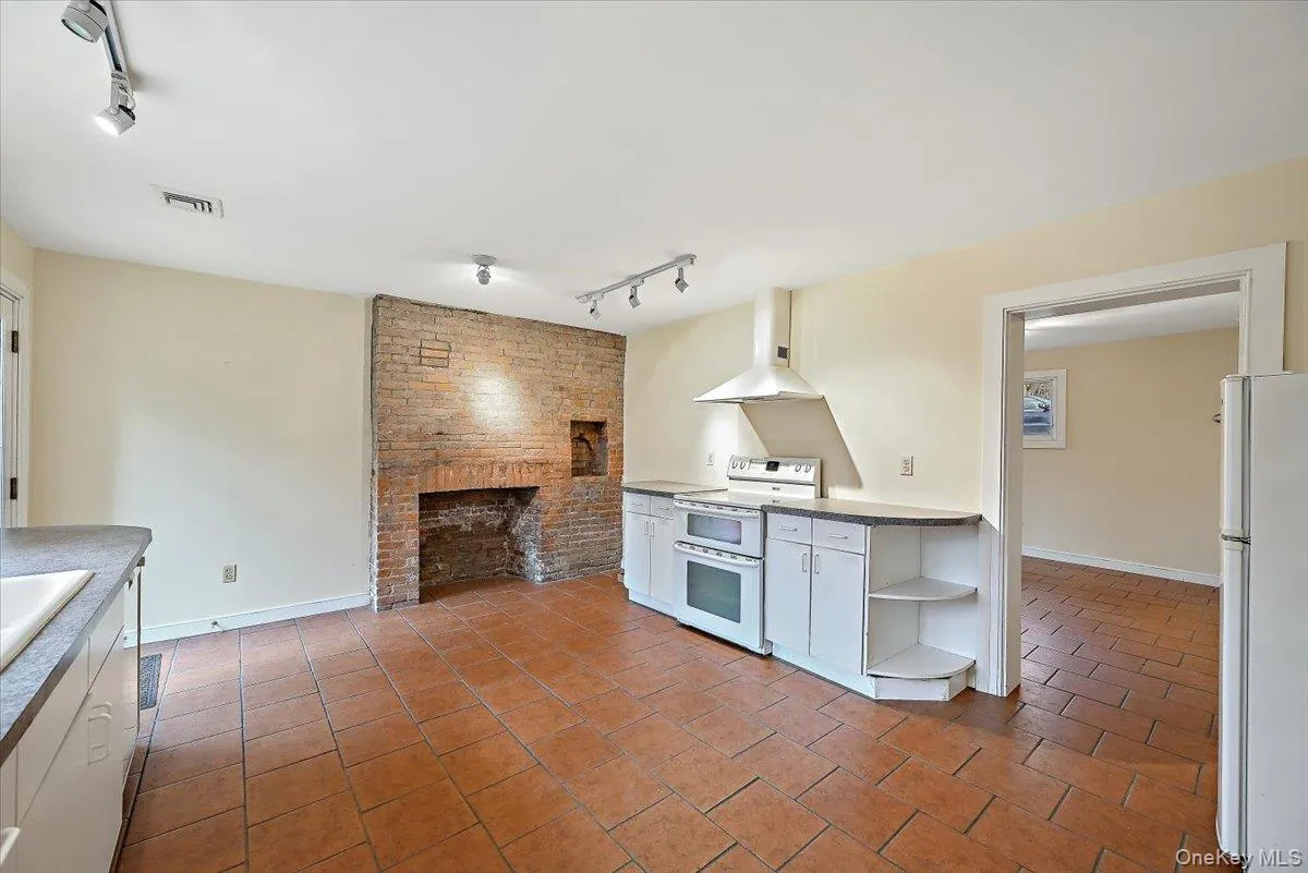 Kitchen with track lighting, white cabinets, white appliances, wall chimney range hood, and light tile patterned floors Kitchen with track lighting, white cabinets, white appliances, wall chimney range hood, and light tile patterned floors