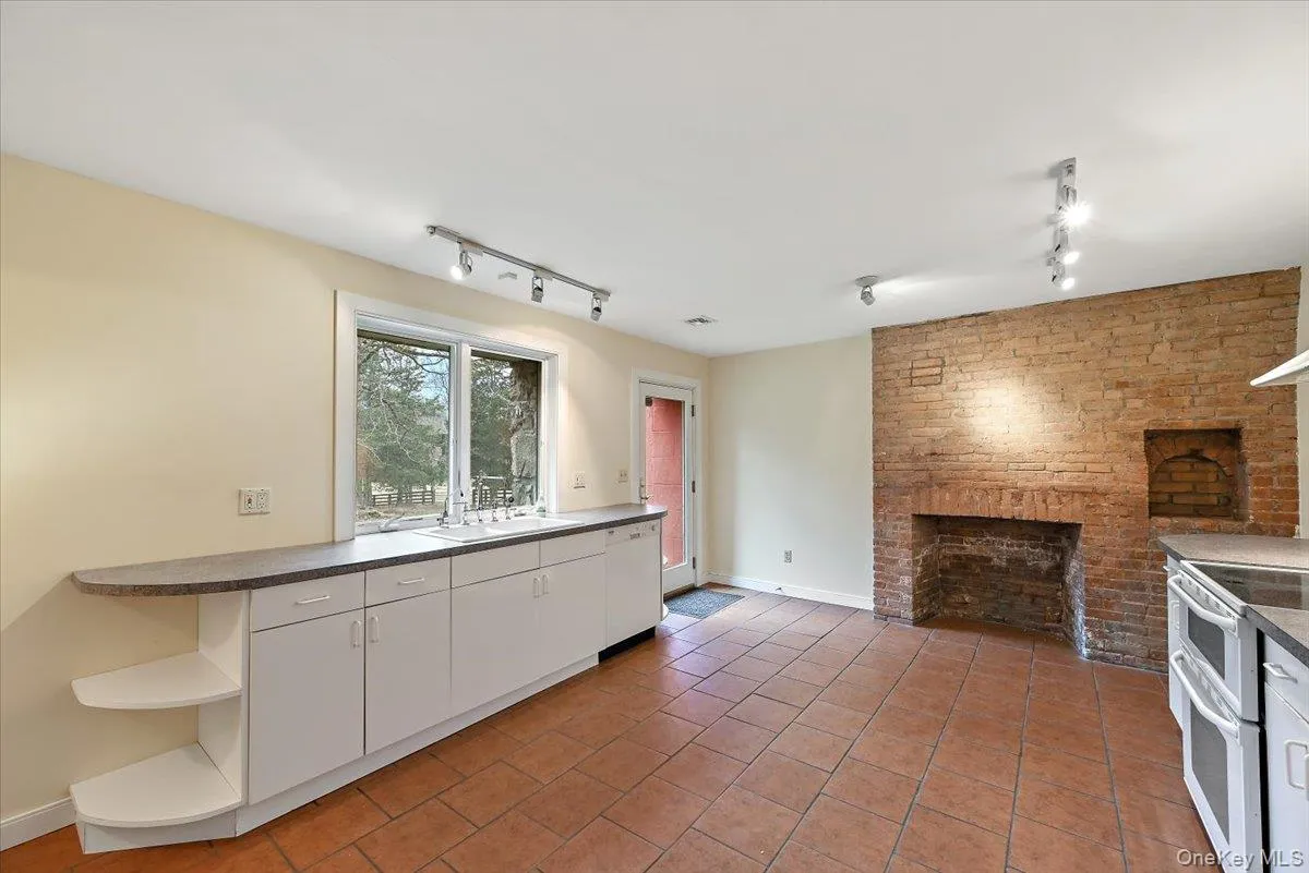 Kitchen with white cabinets, a brick fireplace, white appliances, dark countertops, and light tile patterned flooring Kitchen with white cabinets, a brick fireplace, white appliances, dark countertops, and light tile patterned flooring