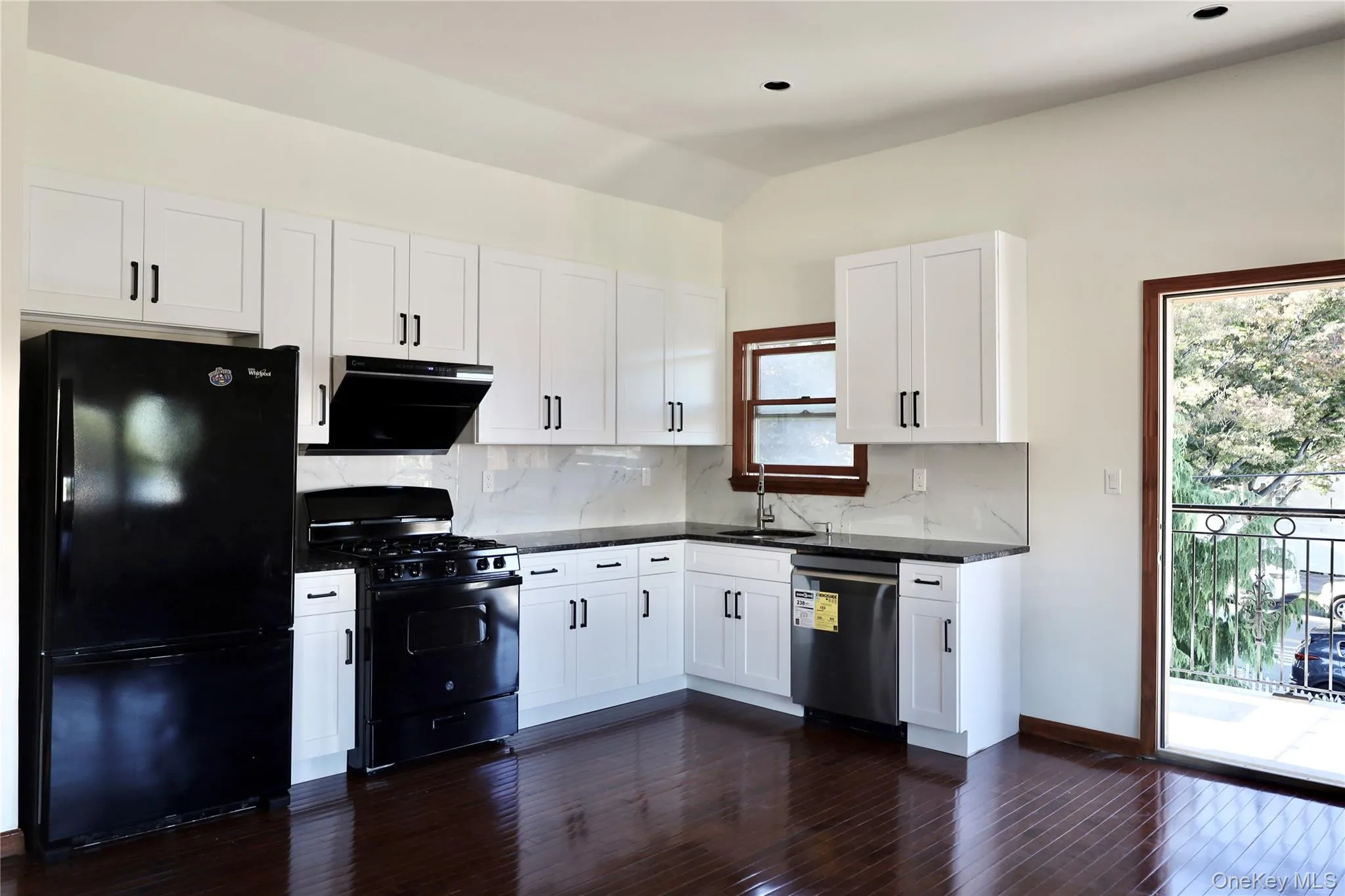 Kitchen featuring black appliances, white cabinets, tasteful backsplash, dark wood-style floors, and ventilation hood Kitchen featuring black appliances, white cabinets, tasteful backsplash, dark wood-style floors, and ventilation hood