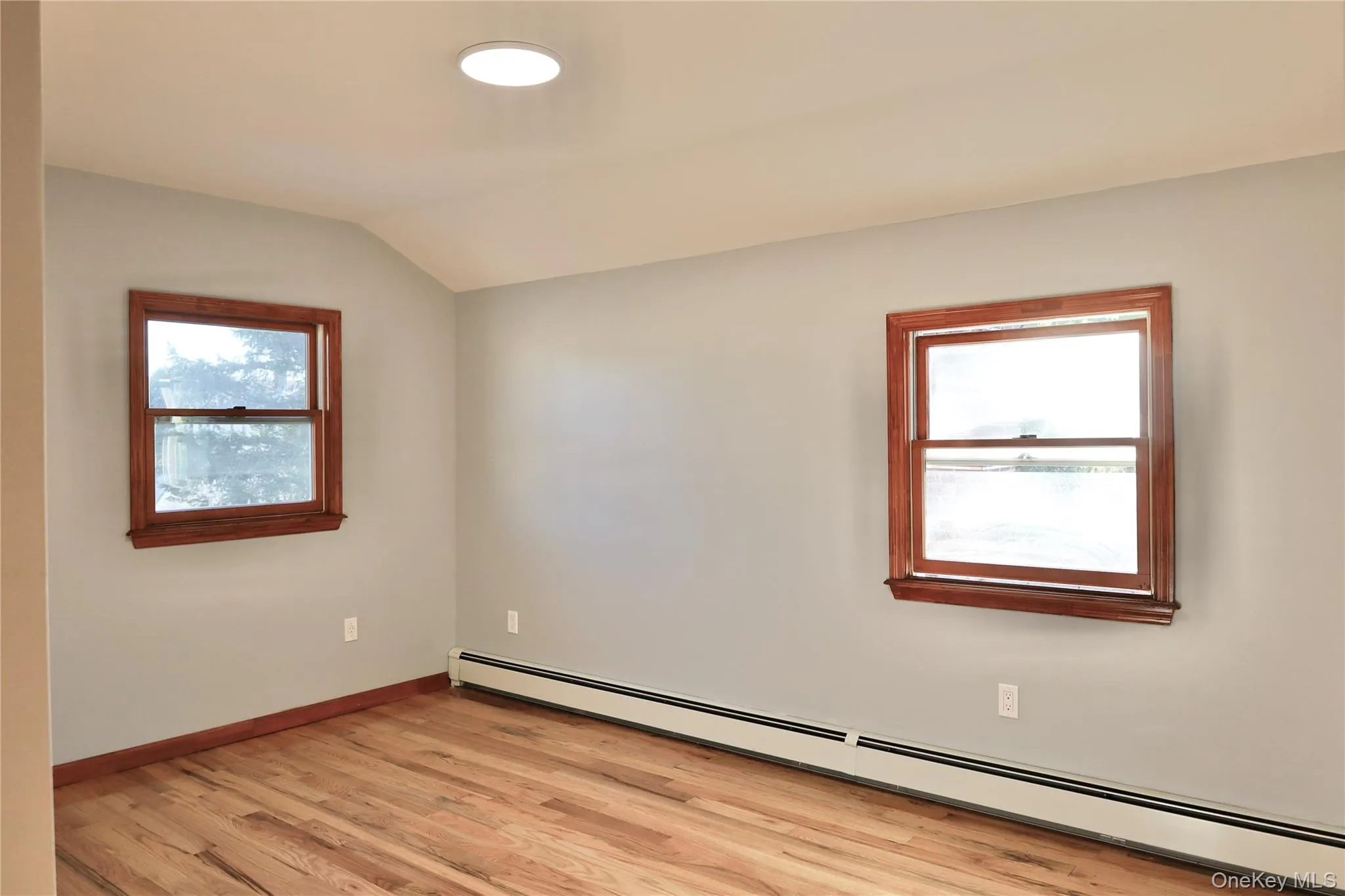 Empty room with a baseboard heating unit, light wood-type flooring, and vaulted ceiling Empty room with a baseboard heating unit, light wood-type flooring, and vaulted ceiling