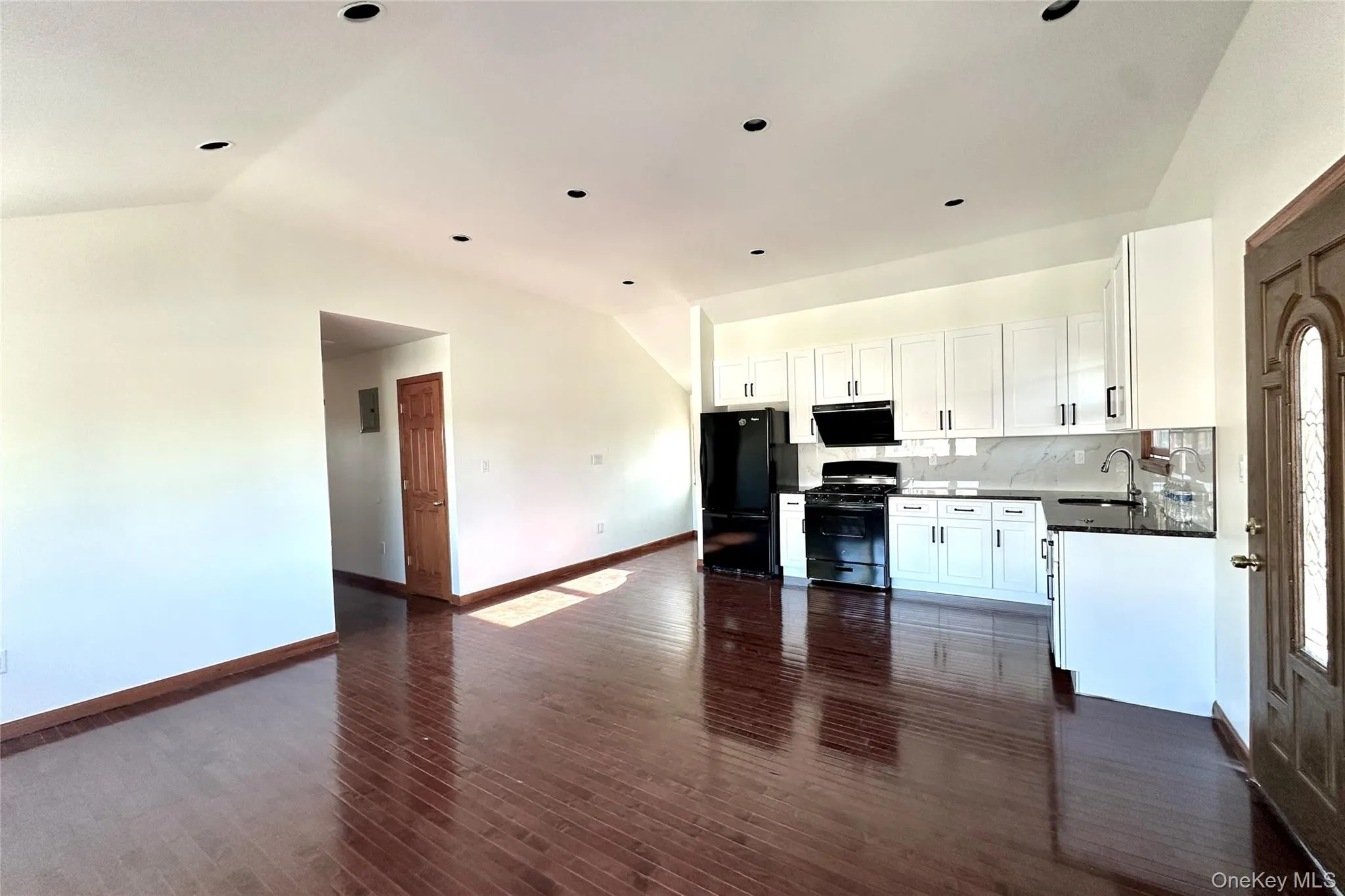 Kitchen featuring white cabinetry, black appliances, decorative backsplash, open floor plan, and dark wood finished floors Kitchen featuring white cabinetry, black appliances, decorative backsplash, open floor plan, and dark wood finished floors