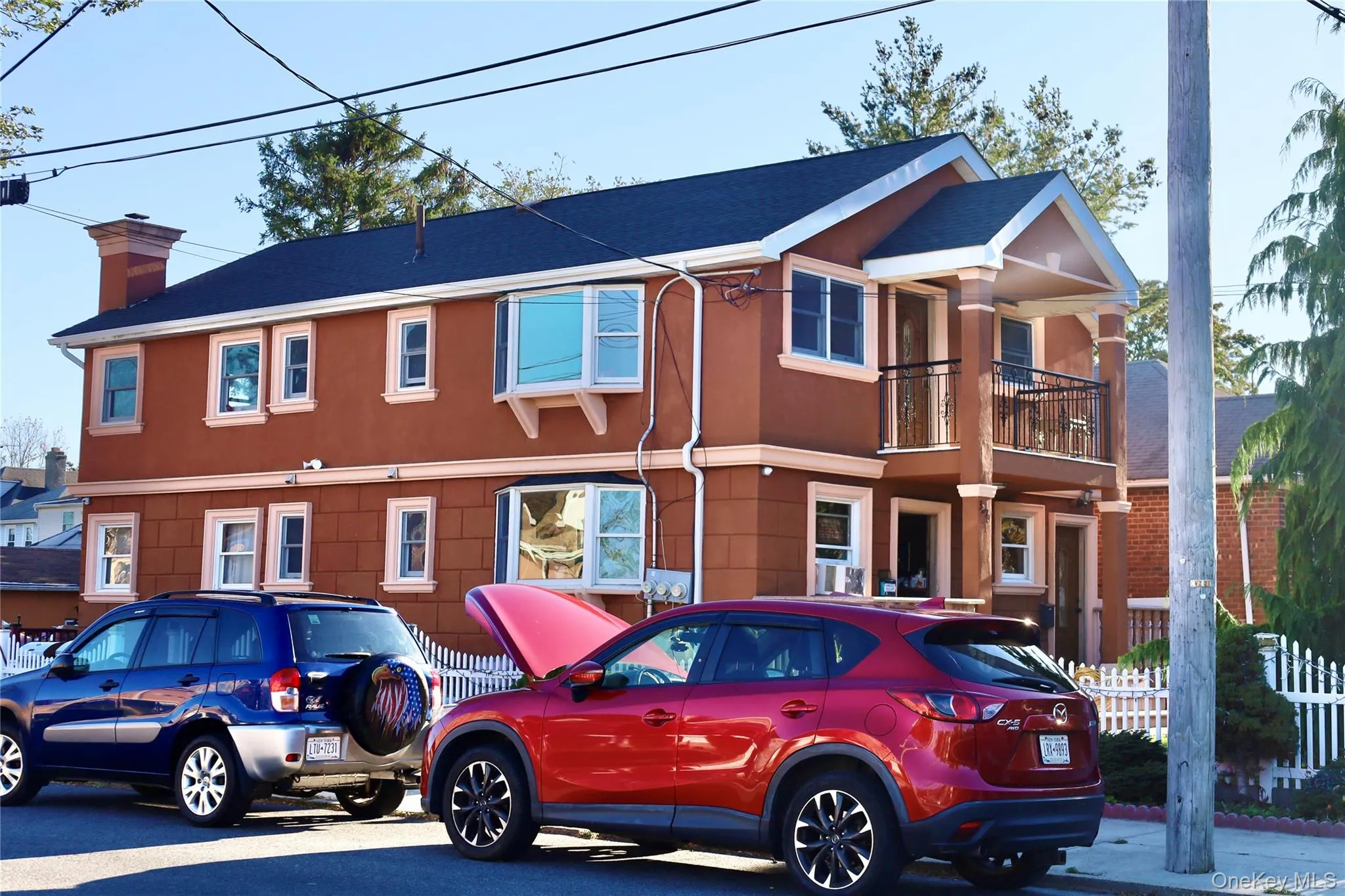 View of front of home featuring a chimney, a balcony, a shingled roof, and stucco siding View of front of home featuring a chimney, a balcony, a shingled roof, and stucco siding