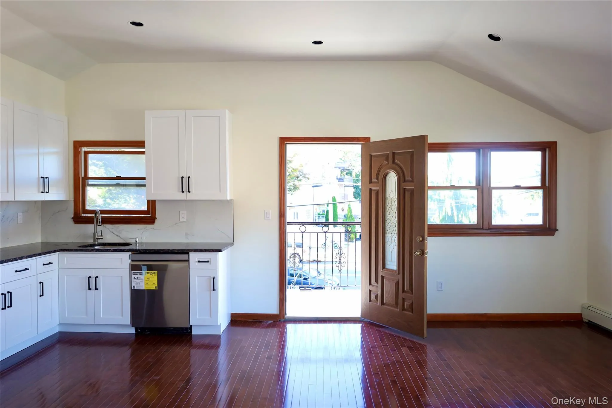 Kitchen featuring lofted ceiling, white cabinetry, stainless steel dishwasher, dark stone counters, and dark wood-type flooring Kitchen featuring lofted ceiling, white cabinetry, stainless steel dishwasher, dark stone counters, and dark wood-type flooring