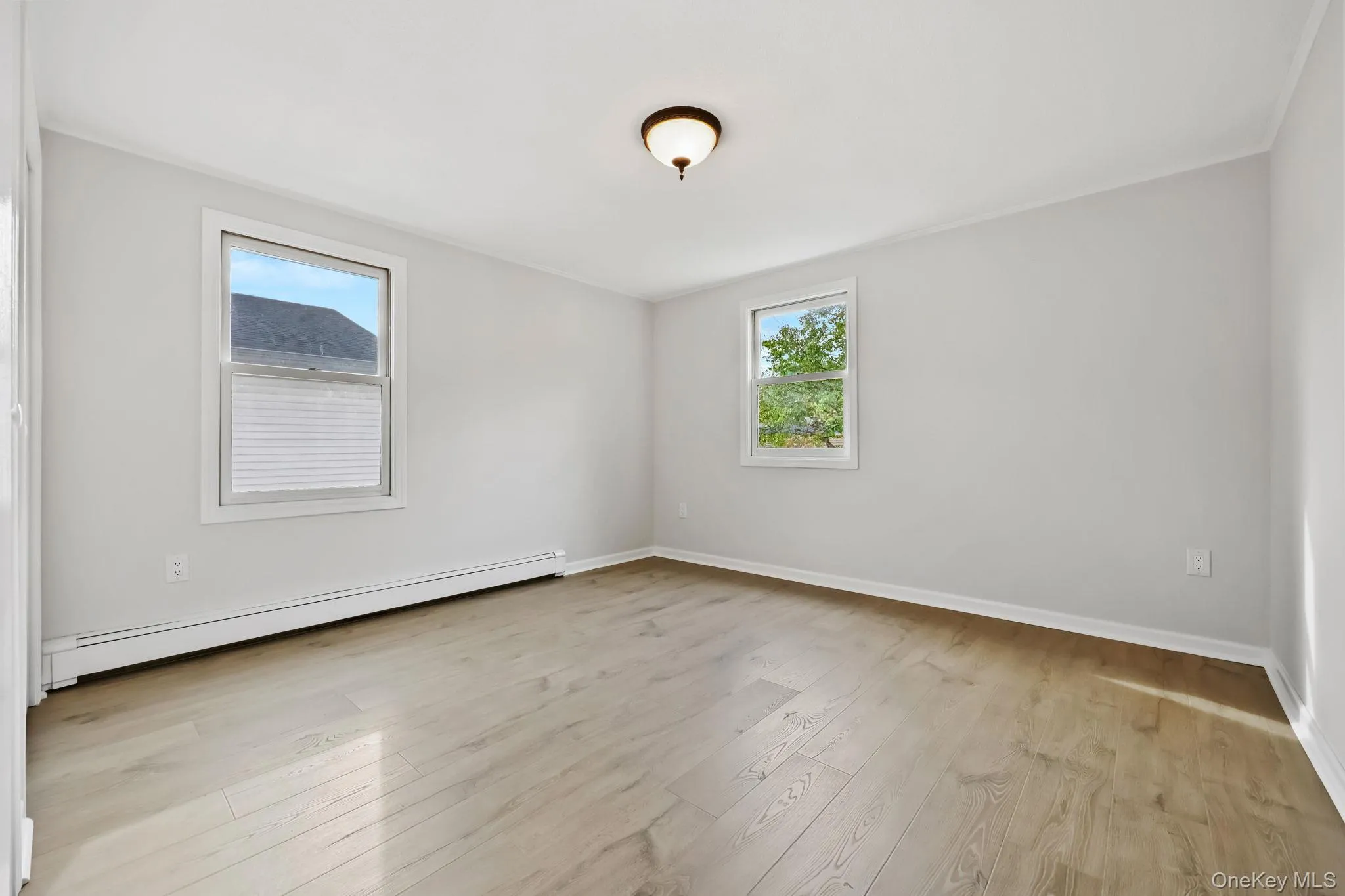 Empty room featuring a baseboard heating unit, light wood finished floors, and healthy amount of natural light Empty room featuring a baseboard heating unit, light wood finished floors, and healthy amount of natural light