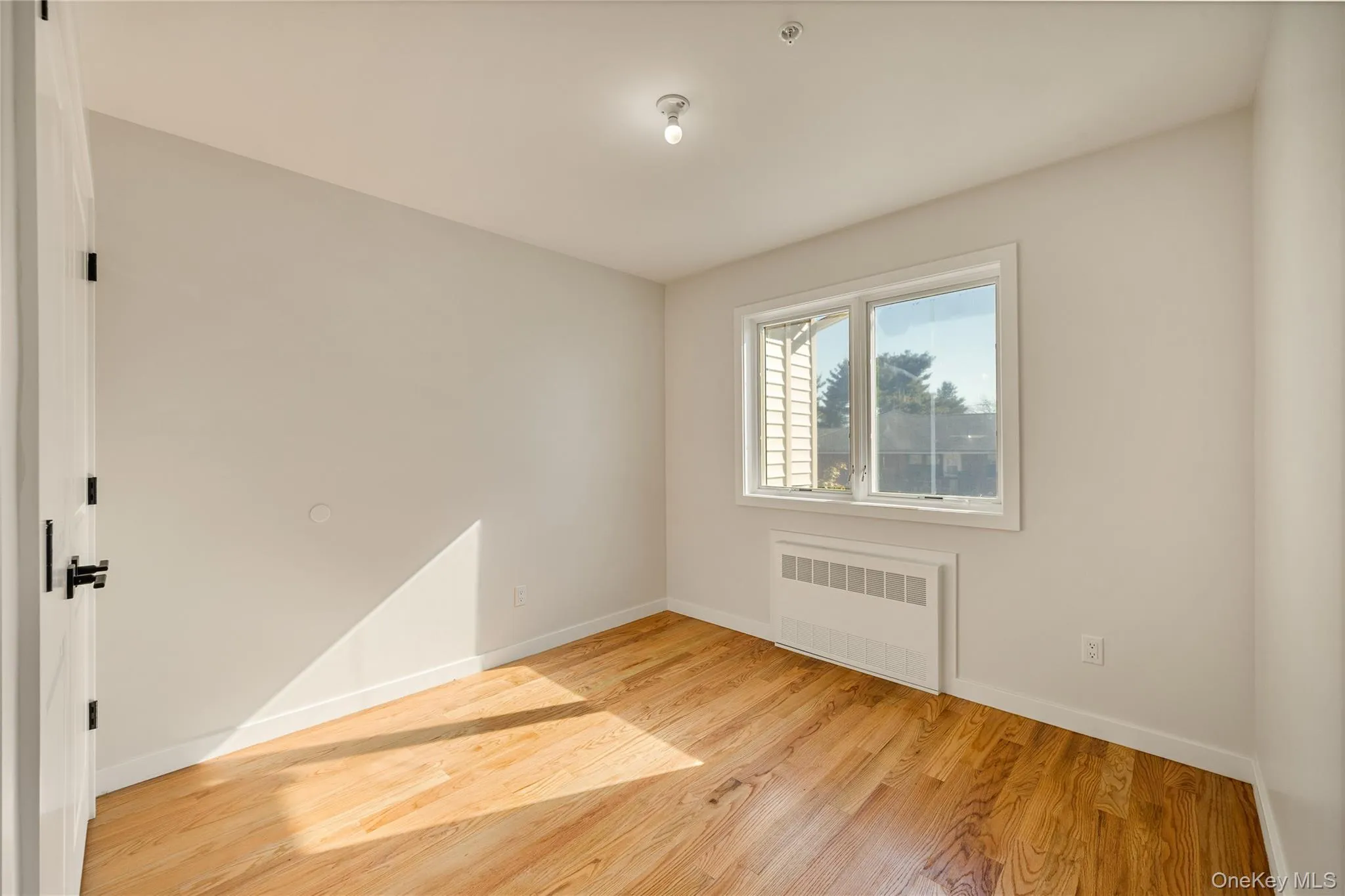 Empty room with radiator heating unit and light wood-style flooring Empty room with radiator heating unit and light wood-style flooring