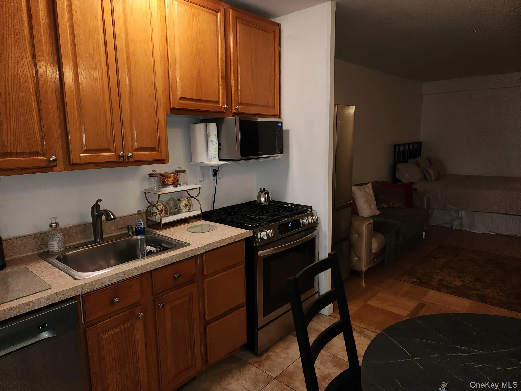 Kitchen with appliances with stainless steel finishes, brown cabinetry, light countertops, light tile patterned floors, and open floor plan Kitchen with appliances with stainless steel finishes, brown cabinetry, light countertops, light tile patterned floors, and open floor plan