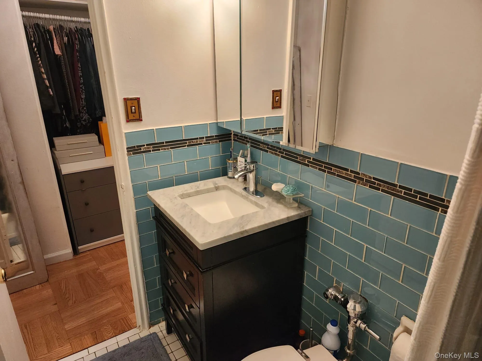 Half bathroom with tile walls, vanity, a walk in closet, a wainscoted wall, and light tile patterned floors Half bathroom with tile walls, vanity, a walk in closet, a wainscoted wall, and light tile patterned floors