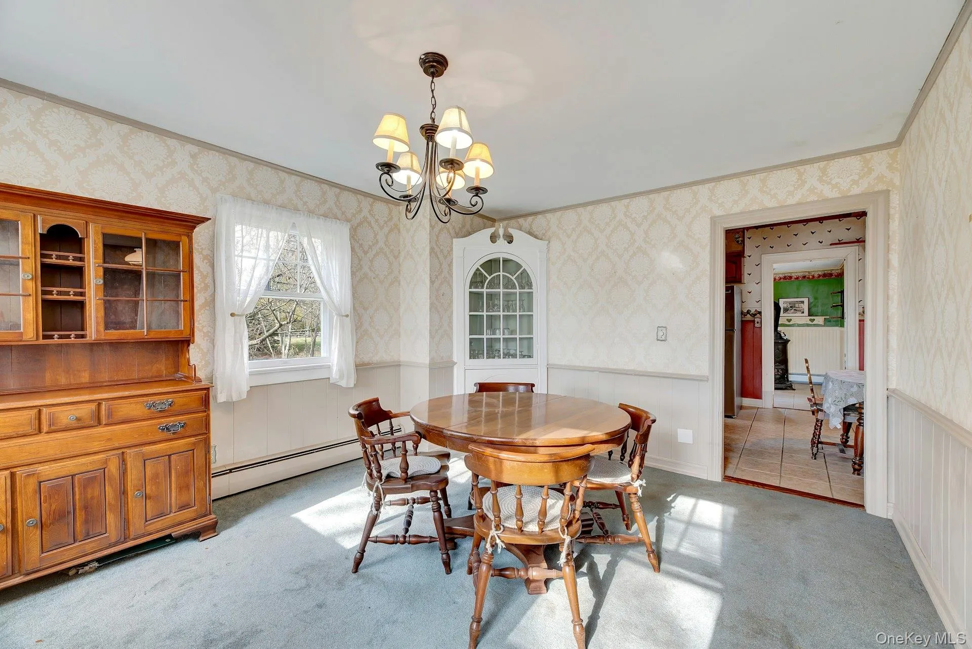 Dining space featuring wallpapered walls, wainscoting, light carpet, a chandelier, and a baseboard radiator Dining space featuring wallpapered walls, wainscoting, light carpet, a chandelier, and a baseboard radiator