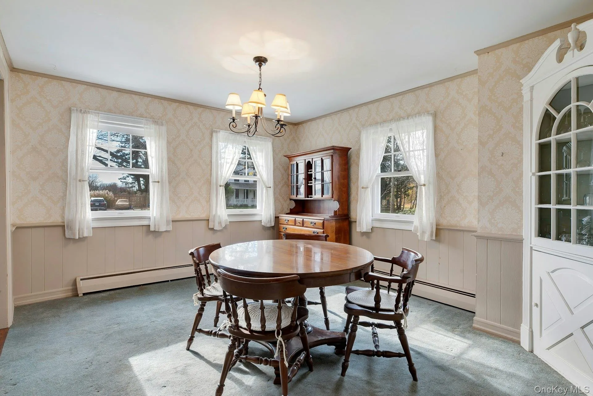 Dining area with wainscoting, wallpapered walls, baseboard heating, carpet floors, and a chandelier Dining area with wainscoting, wallpapered walls, baseboard heating, carpet floors, and a chandelier