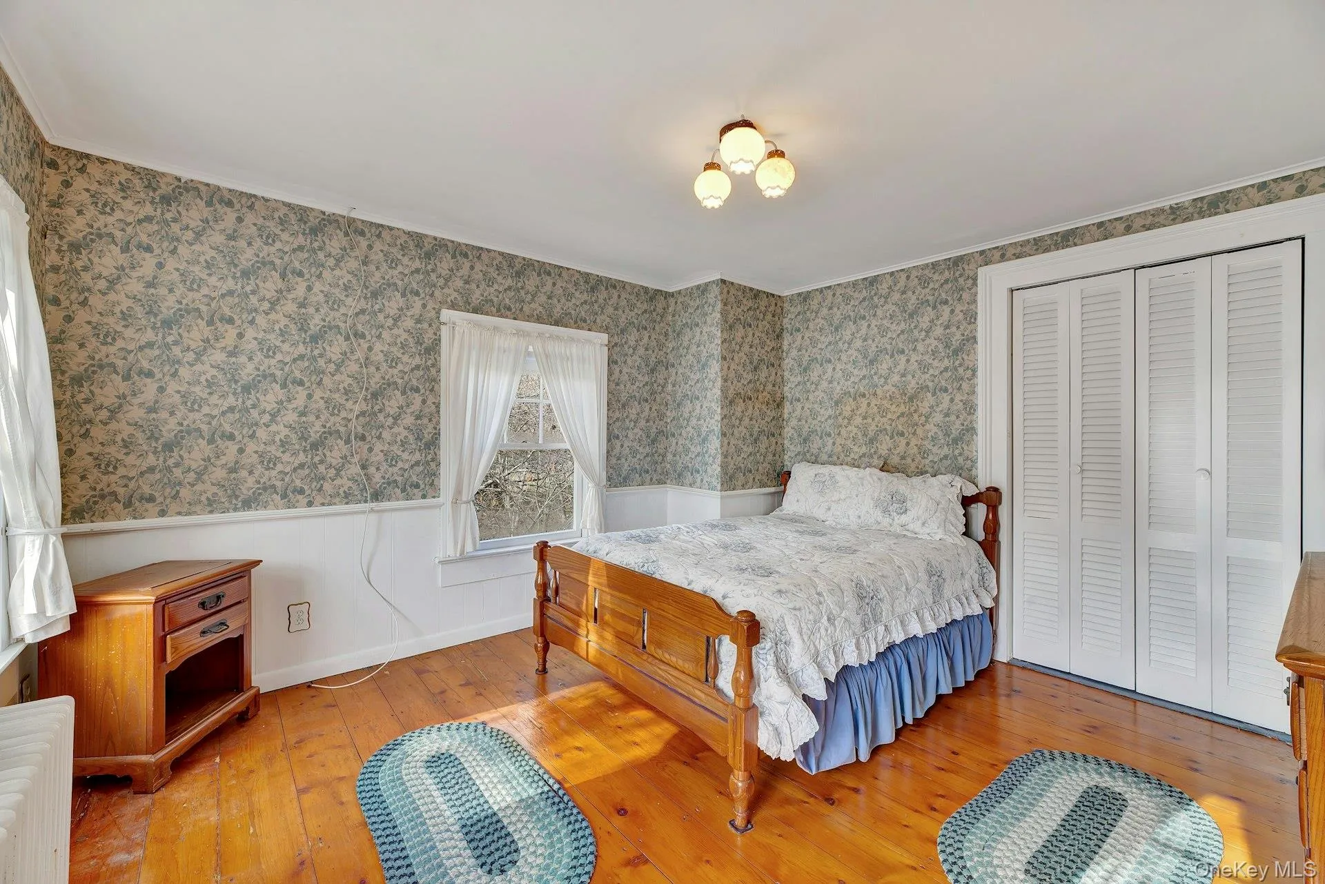 Bedroom with a wainscoted wall, wallpapered walls, wood-type flooring, and a closet Bedroom with a wainscoted wall, wallpapered walls, wood-type flooring, and a closet