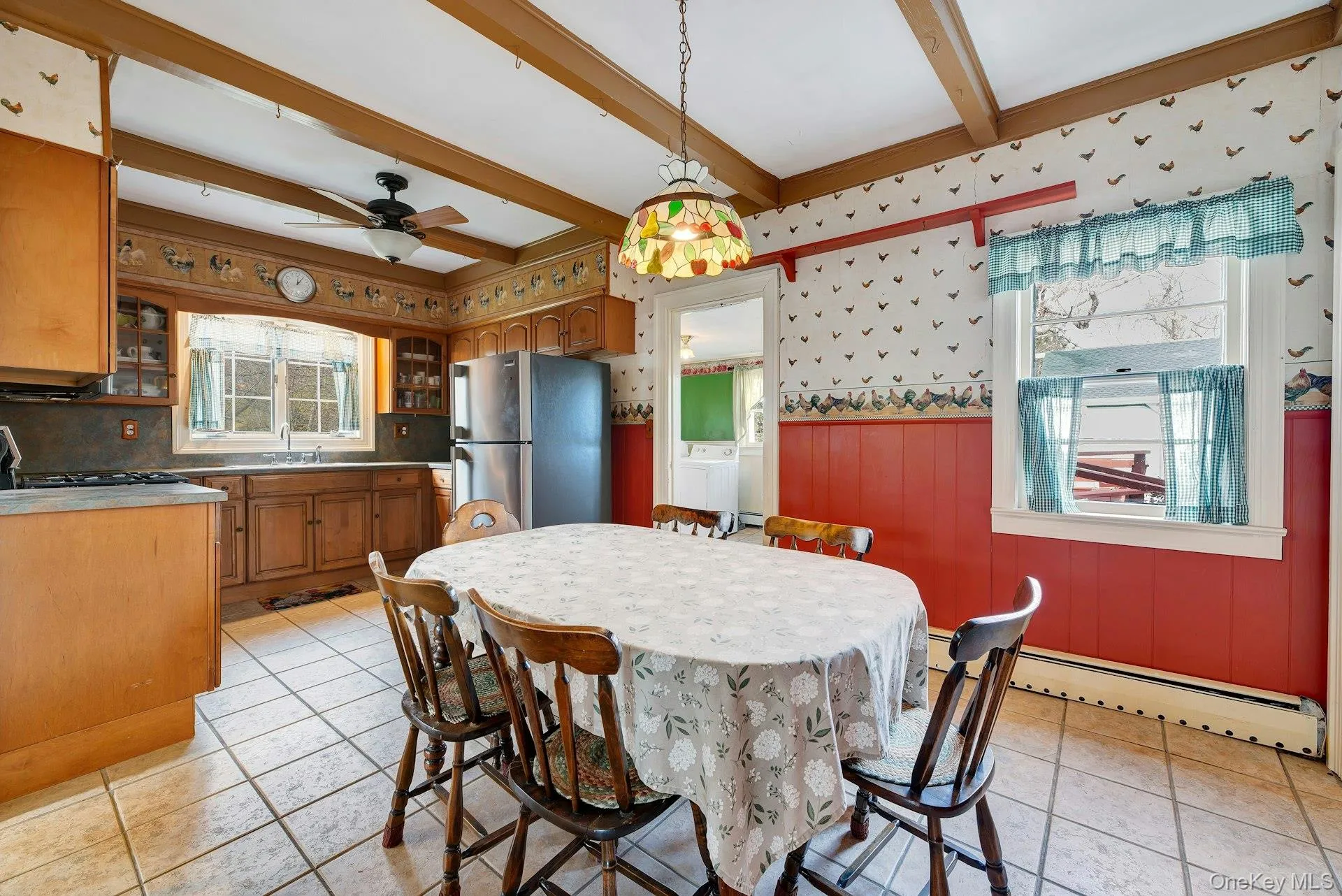 Dining space with a wainscoted wall, a ceiling fan, a baseboard heating unit, wallpapered walls, and beamed ceiling Dining space with a wainscoted wall, a ceiling fan, a baseboard heating unit, wallpapered walls, and beamed ceiling