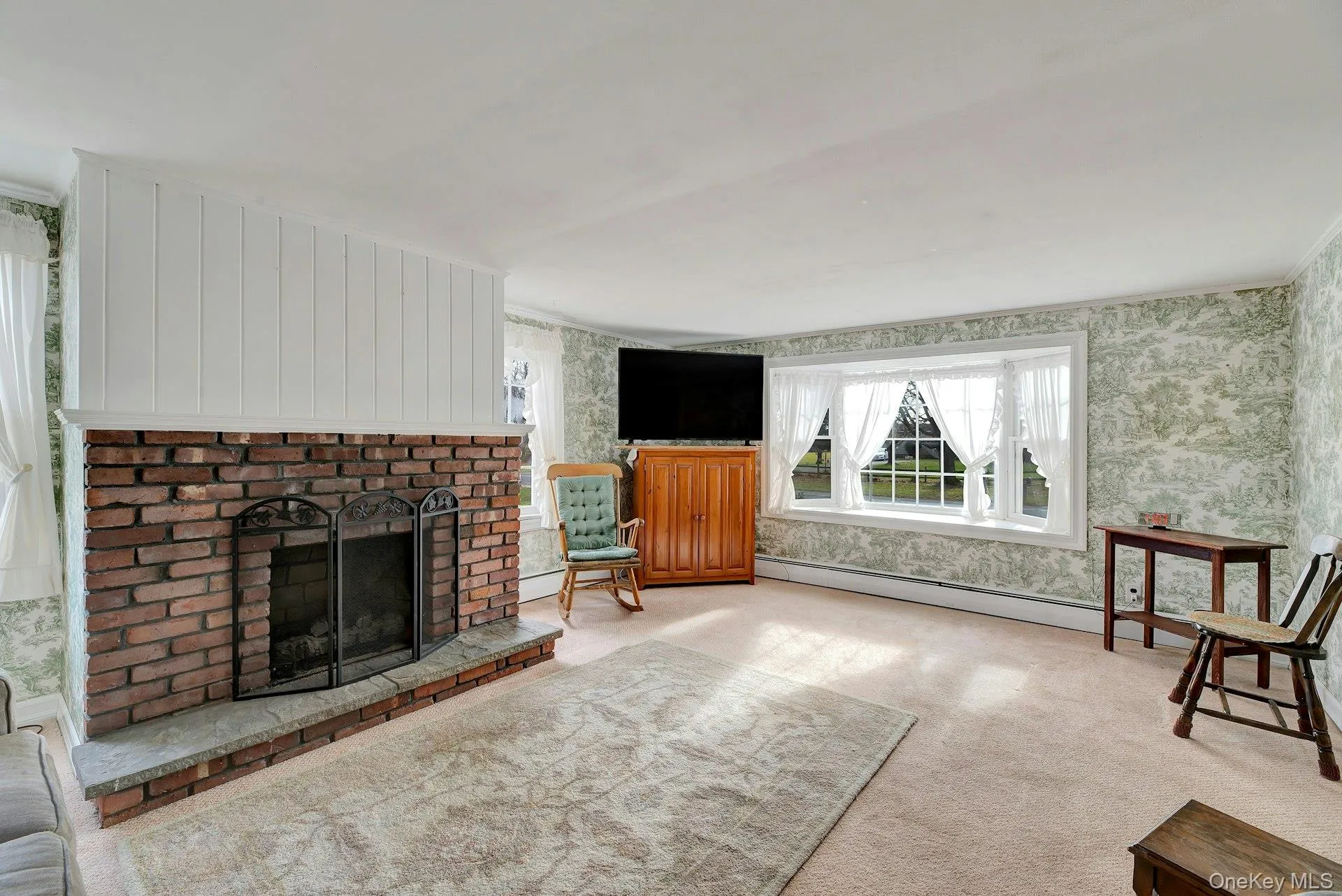 Unfurnished living room featuring a fireplace, wallpapered walls, a baseboard radiator, healthy amount of natural light, and carpet Unfurnished living room featuring a fireplace, wallpapered walls, a baseboard radiator, healthy amount of natural light, and carpet