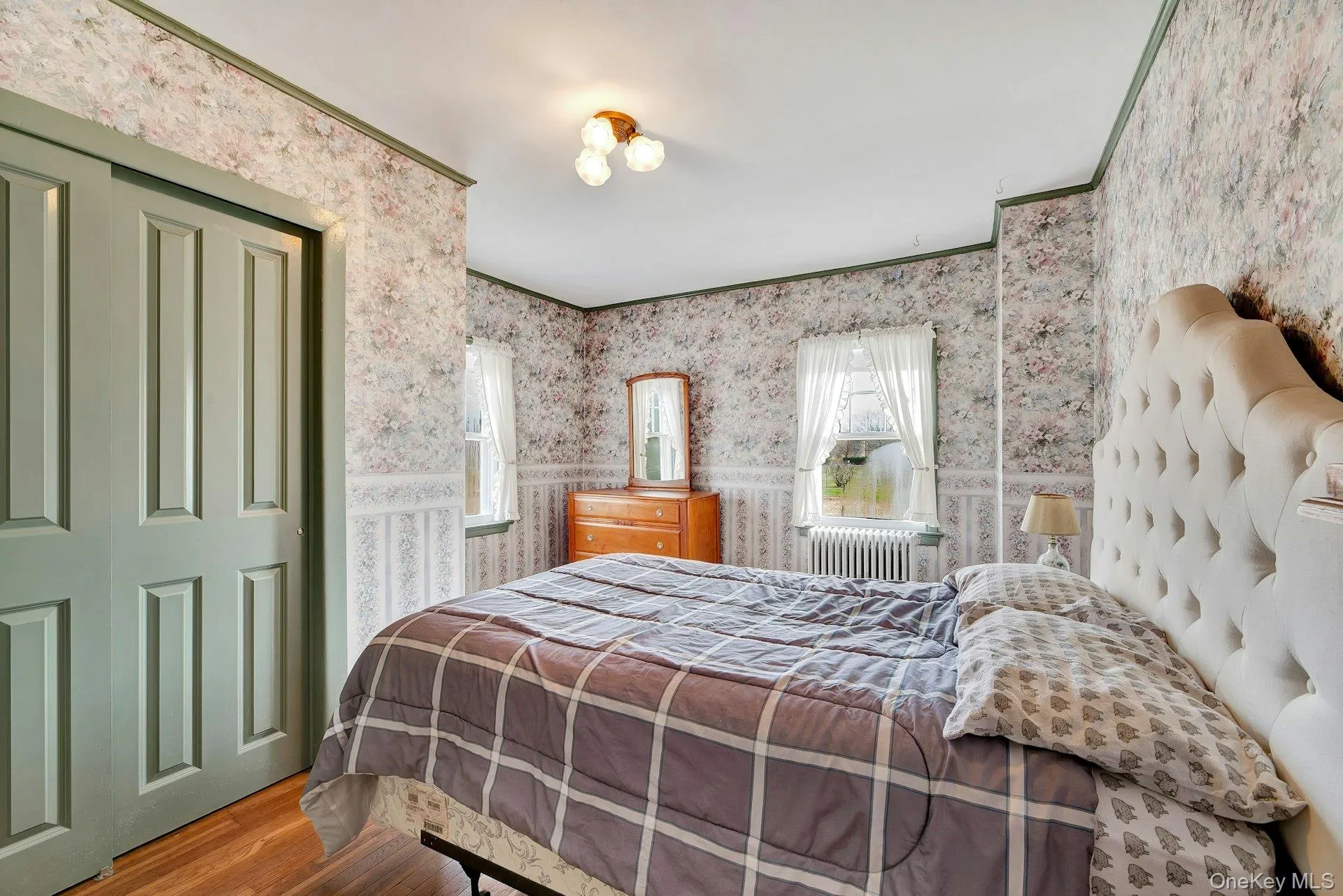 Bedroom featuring wood finished floors, wallpapered walls, a closet, and radiator heating unit Bedroom featuring wood finished floors, wallpapered walls, a closet, and radiator heating unit