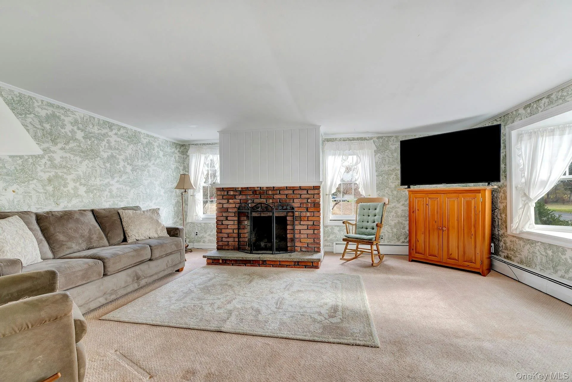 Living room featuring wallpapered walls, a fireplace, carpet floors, and a baseboard radiator Living room featuring wallpapered walls, a fireplace, carpet floors, and a baseboard radiator