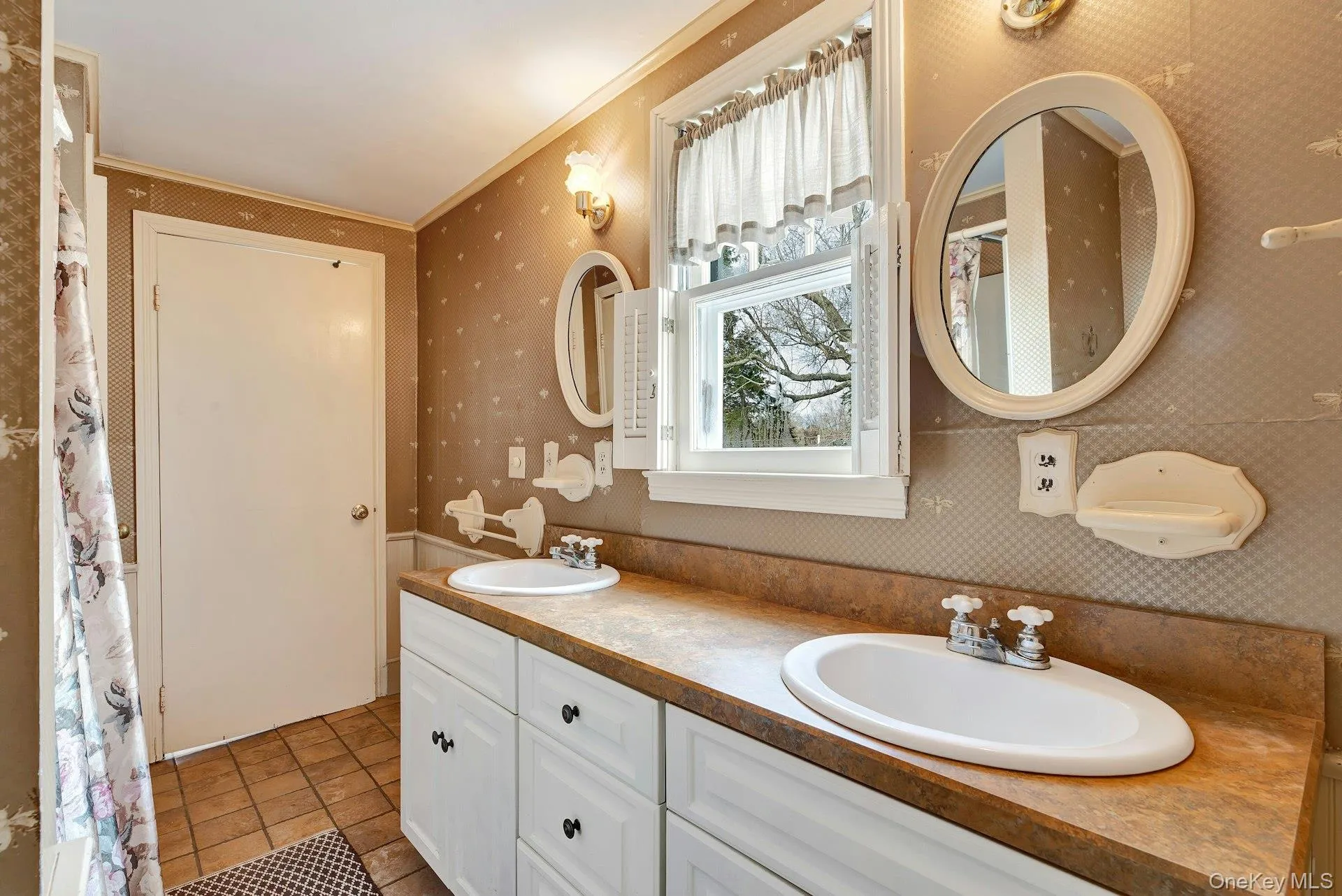 Bathroom with wallpapered walls, double vanity, light tile patterned floors, curtained shower, and ornamental molding Bathroom with wallpapered walls, double vanity, light tile patterned floors, curtained shower, and ornamental molding
