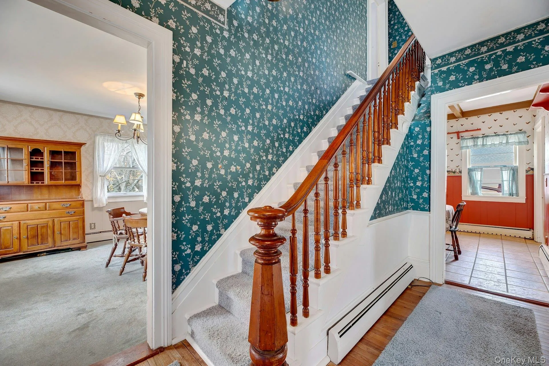 Staircase with wallpapered walls, a baseboard heating unit, a chandelier, wood finished floors, and a wainscoted wall Staircase with wallpapered walls, a baseboard heating unit, a chandelier, wood finished floors, and a wainscoted wall