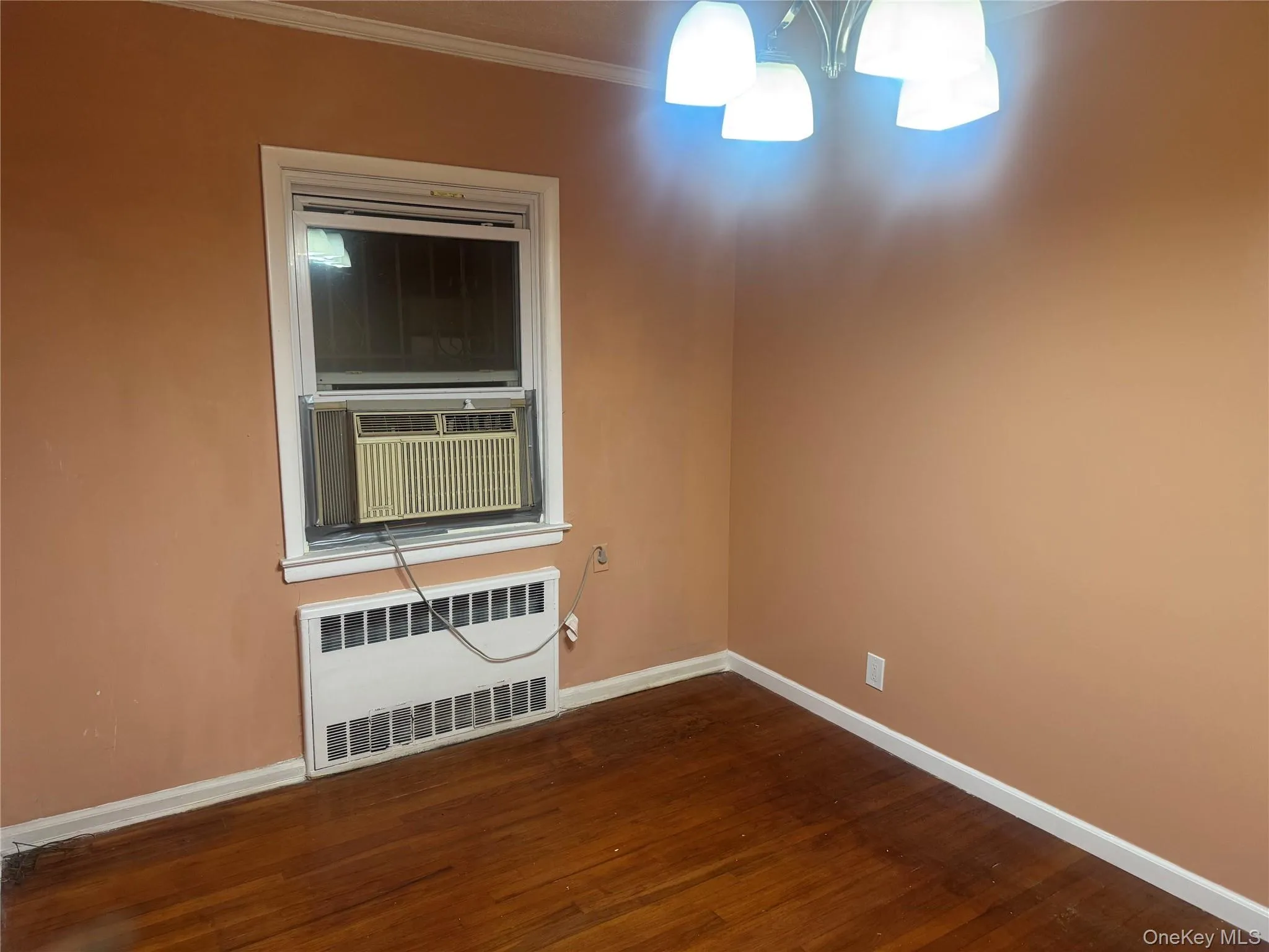 Unfurnished room featuring radiator, ornamental molding, dark wood-style floors, and cooling unit Unfurnished room featuring radiator, ornamental molding, dark wood-style floors, and cooling unit