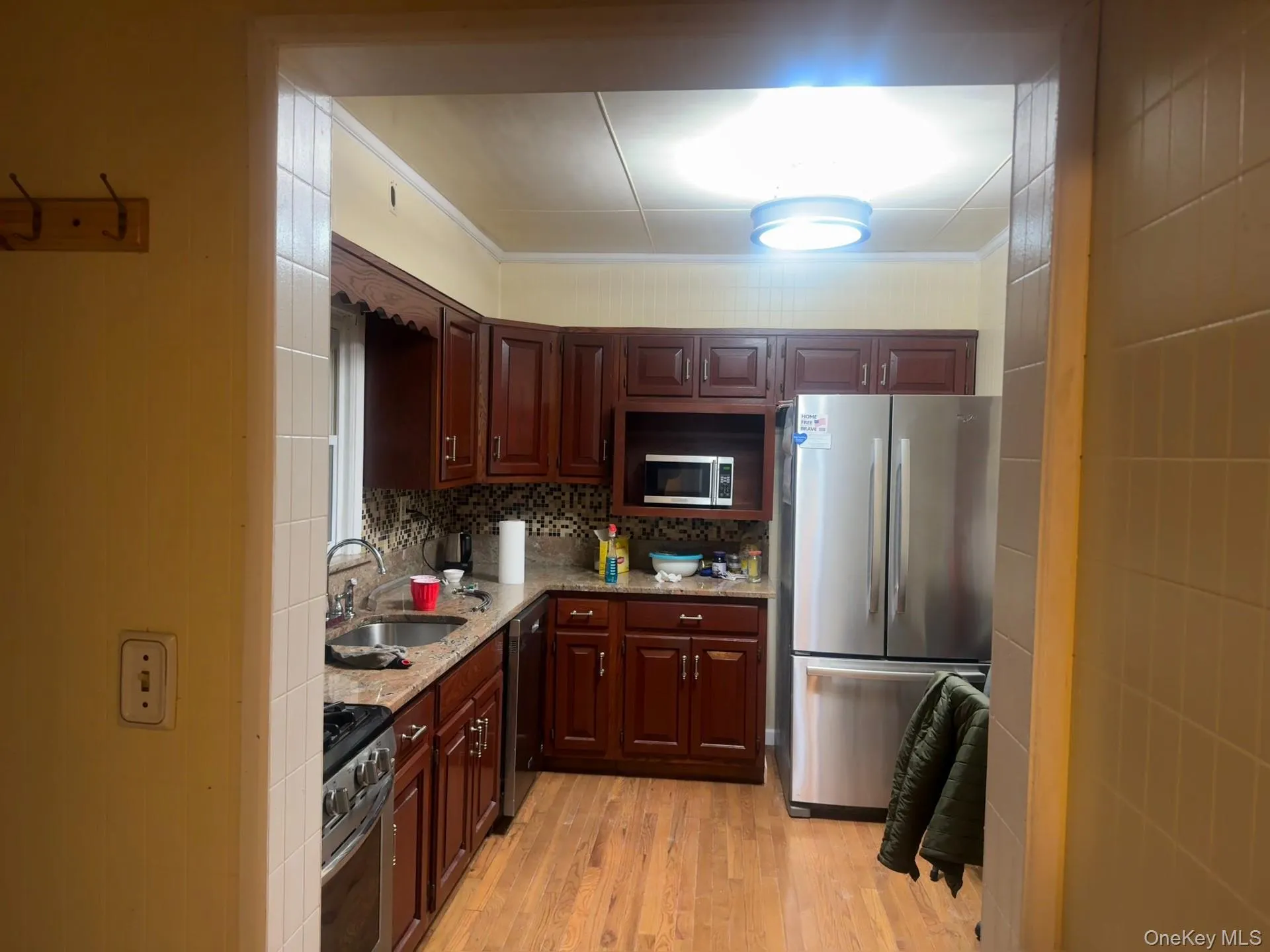 Kitchen with appliances with stainless steel finishes, light wood finished floors, tasteful backsplash, light stone countertops, and ornamental molding Kitchen with appliances with stainless steel finishes, light wood finished floors, tasteful backsplash, light stone countertops, and ornamental molding