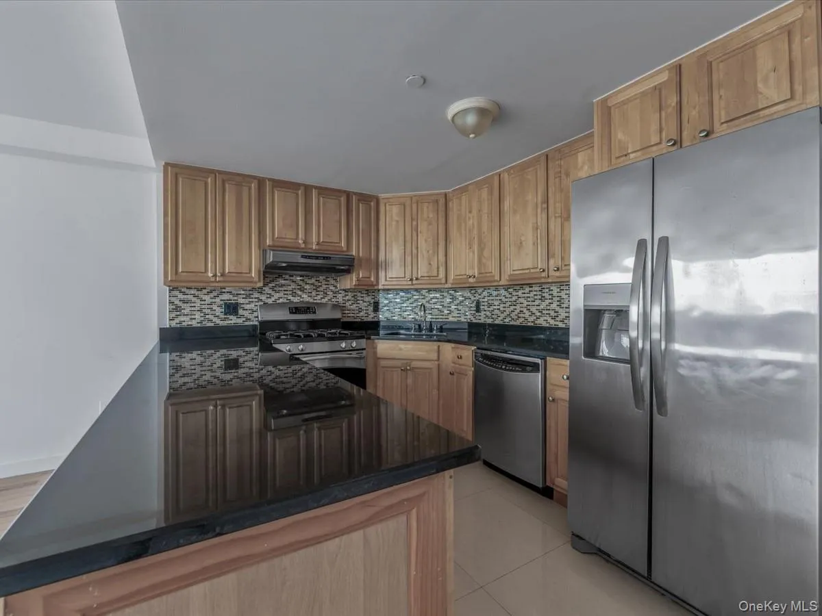 Kitchen with appliances with stainless steel finishes, backsplash, light tile patterned floors, and dark stone counters Kitchen with appliances with stainless steel finishes, backsplash, light tile patterned floors, and dark stone counters