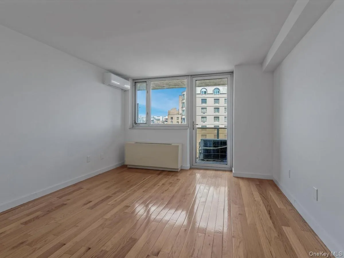 Unfurnished room with radiator, light wood finished floors, and a wall mounted air conditioner Unfurnished room with radiator, light wood finished floors, and a wall mounted air conditioner