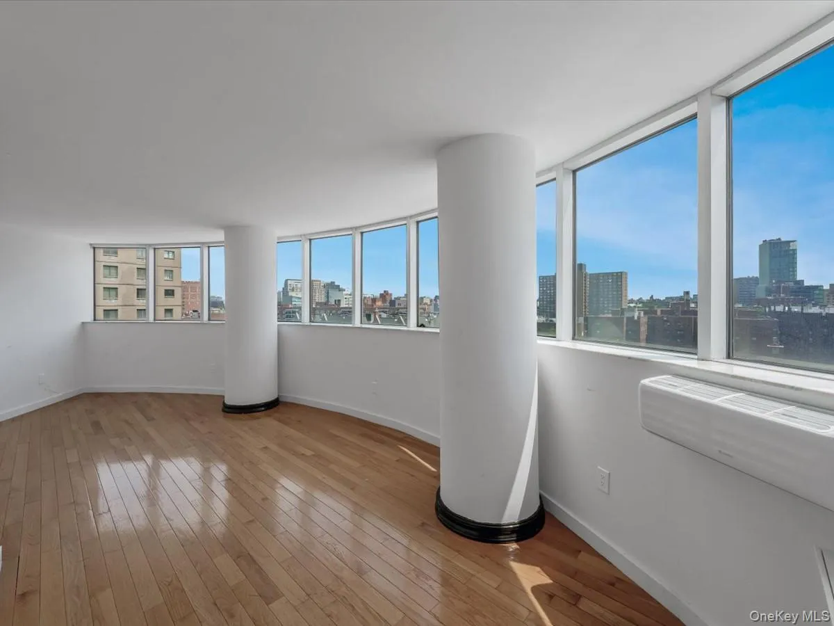 Empty room featuring a skyline view, light wood-style floors, and an AC wall unit Empty room featuring a skyline view, light wood-style floors, and an AC wall unit