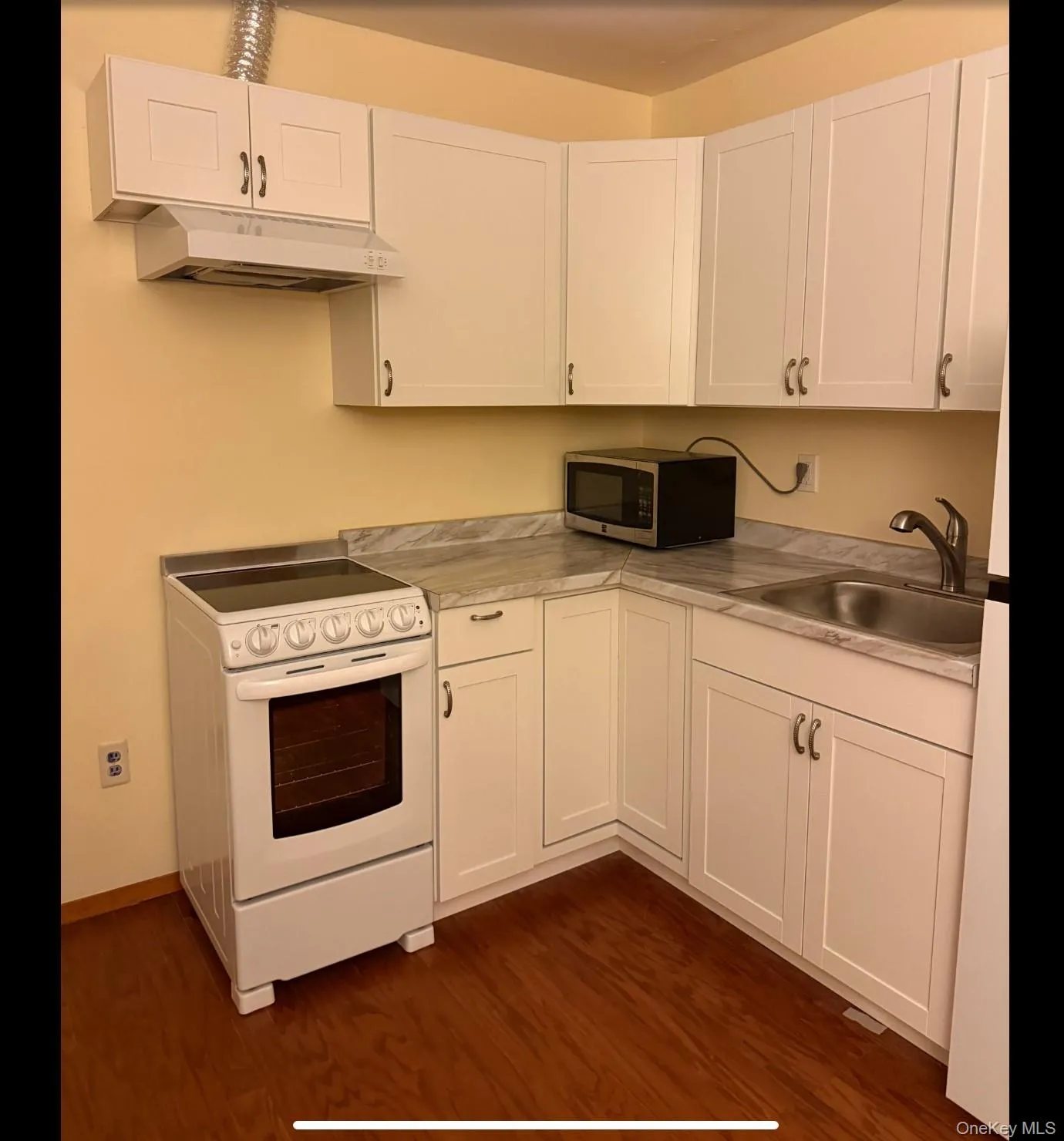Kitchen with white range with electric cooktop, white cabinetry, stainless steel microwave, under cabinet range hood, and light countertops Kitchen with white range with electric cooktop, white cabinetry, stainless steel microwave, under cabinet range hood, and light countertops
