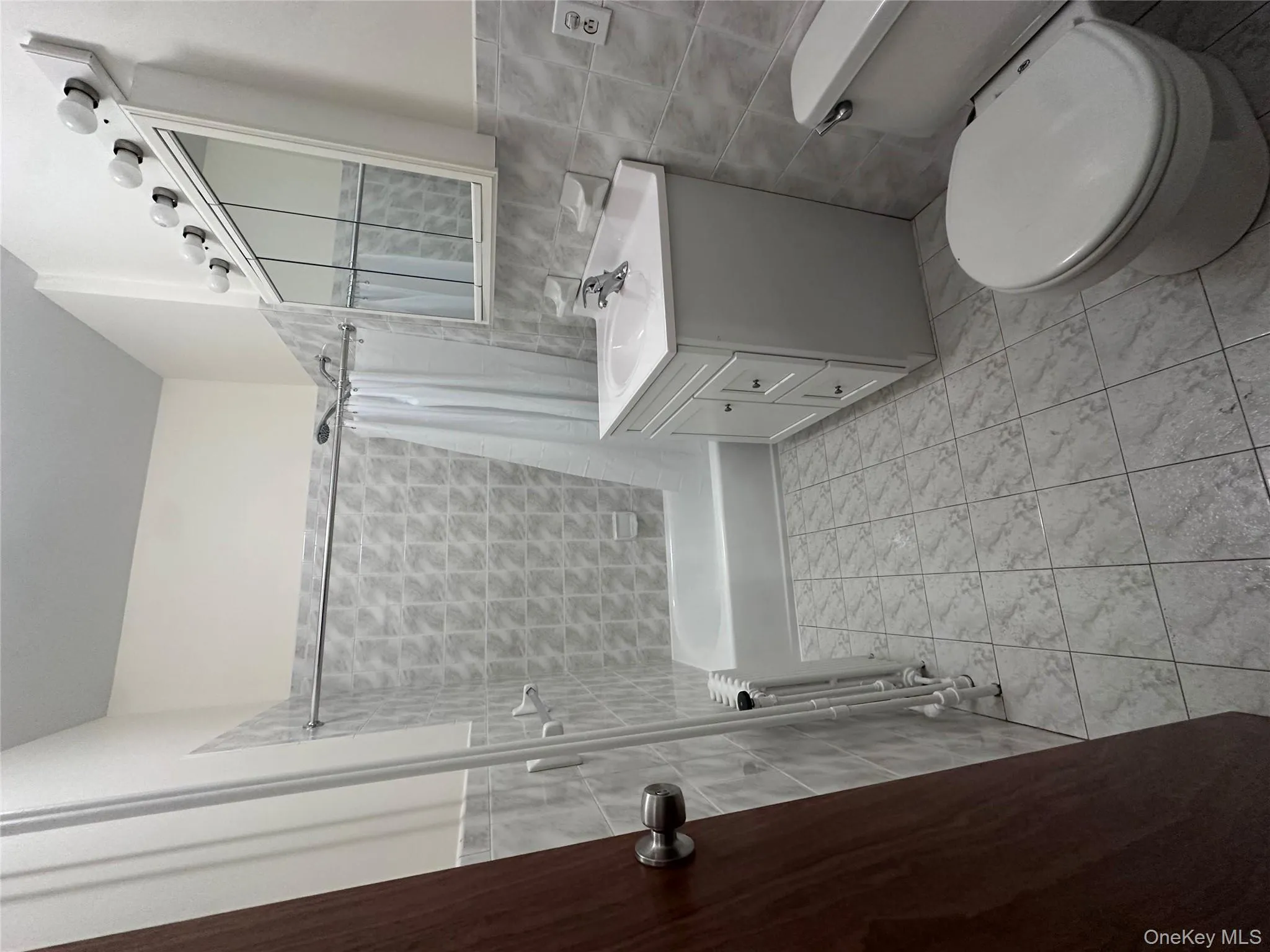 Bathroom with tile walls, vanity, shower / tub combo, light tile patterned flooring, and radiator heating unit Bathroom with tile walls, vanity, shower / tub combo, light tile patterned flooring, and radiator heating unit