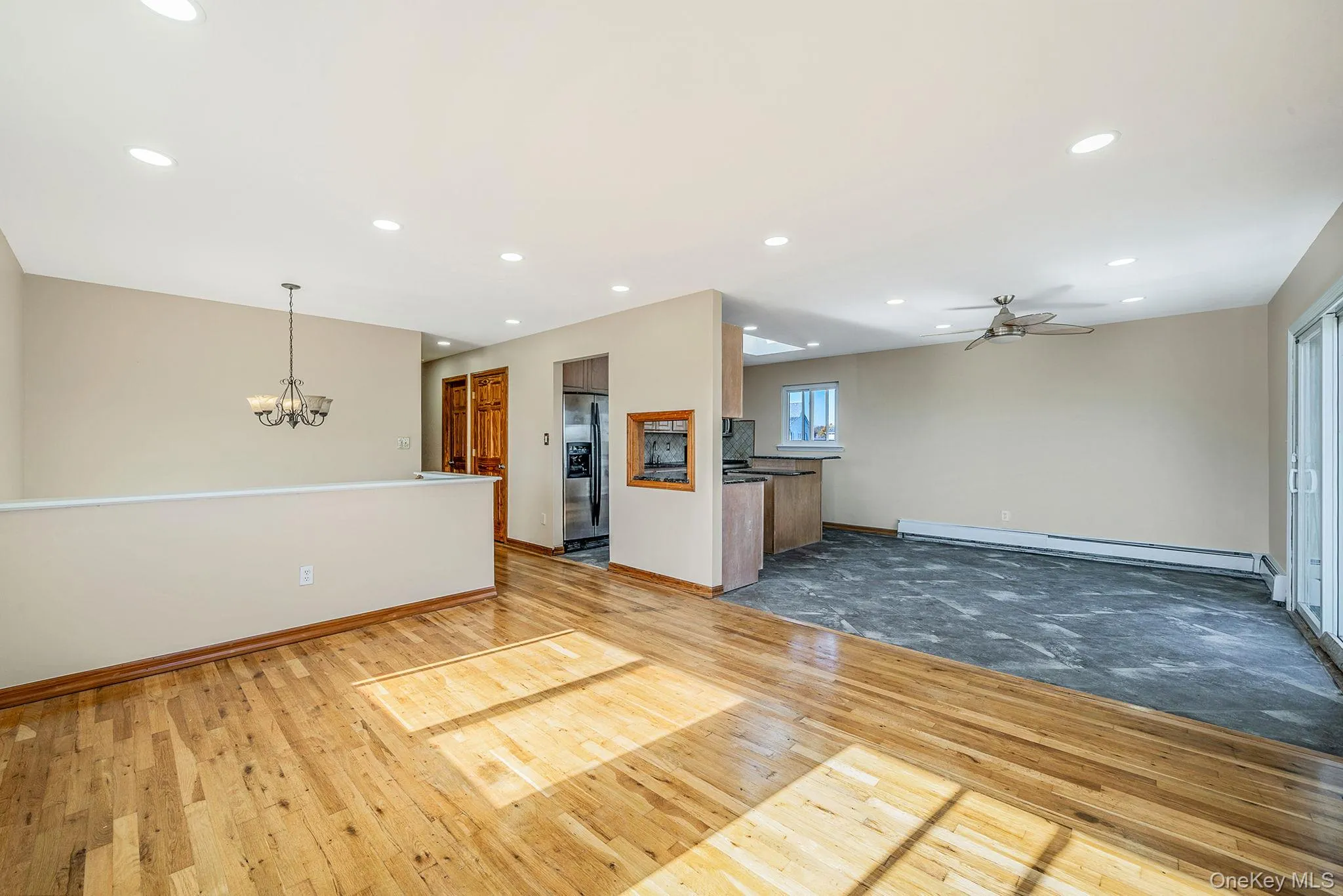 Unfurnished living room featuring light wood-type flooring, ceiling fan, recessed lighting, a chandelier, and a baseboard radiator Unfurnished living room featuring light wood-type flooring, ceiling fan, recessed lighting, a chandelier, and a baseboard radiator