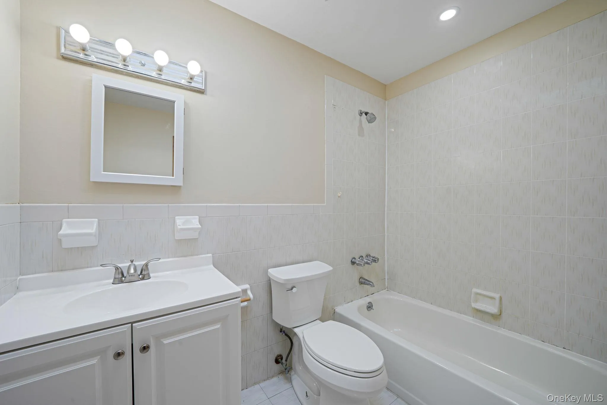 Full bath with tile walls, bathtub / shower combination, vanity, light tile patterned floors, and a wainscoted wall Full bath with tile walls, bathtub / shower combination, vanity, light tile patterned floors, and a wainscoted wall
