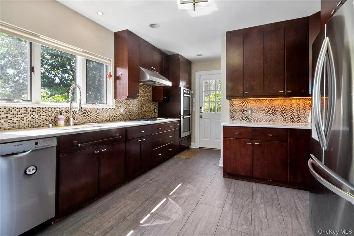 Kitchen featuring appliances with stainless steel finishes, light countertops, under cabinet range hood, and dark brown cabinets Kitchen featuring appliances with stainless steel finishes, light countertops, under cabinet range hood, and dark brown cabinets